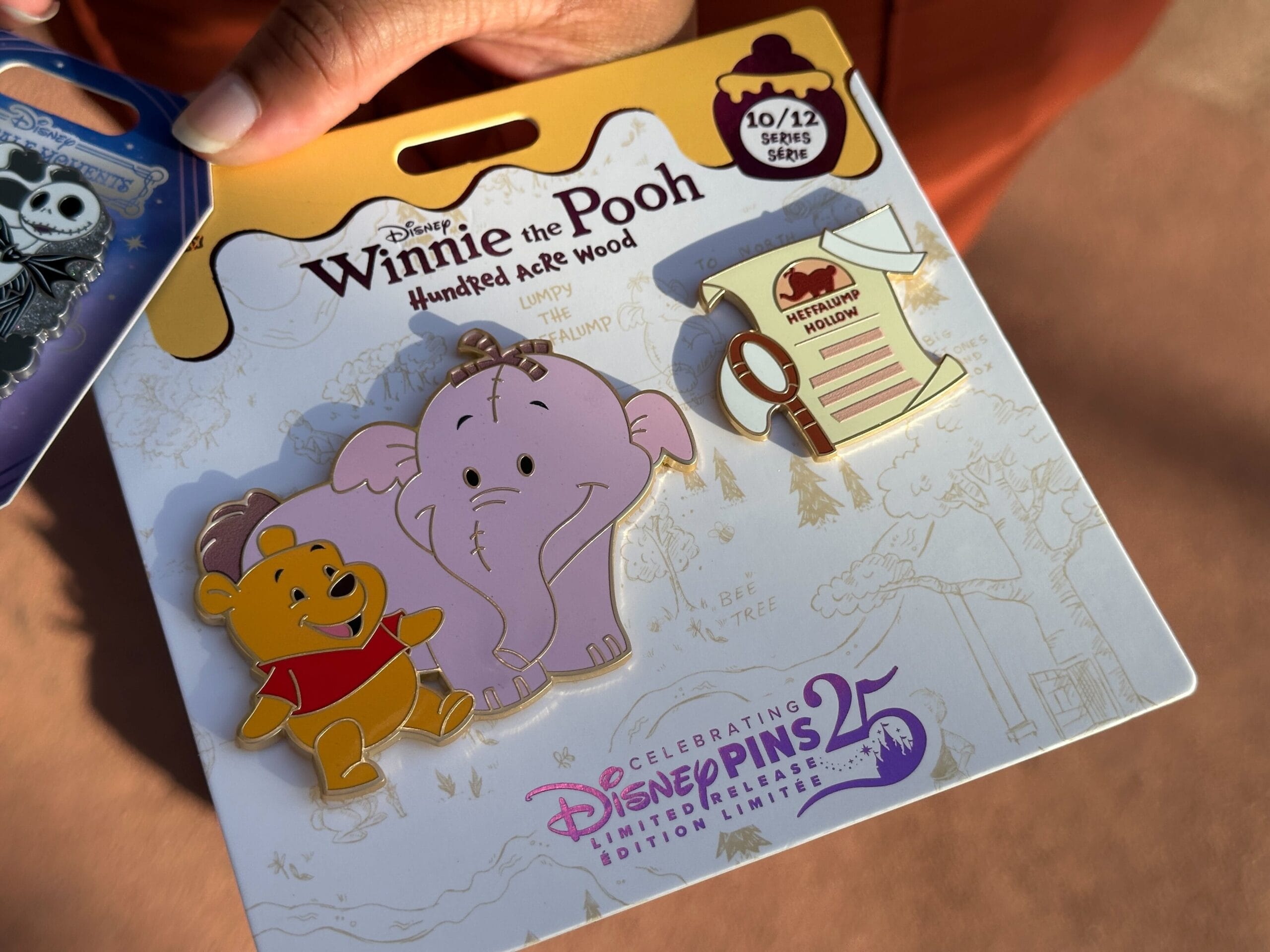 Hand holding a Winnie the Pooh pin set featuring Pooh, Heffalump, and a honey pot note—perfect for Disney fans.