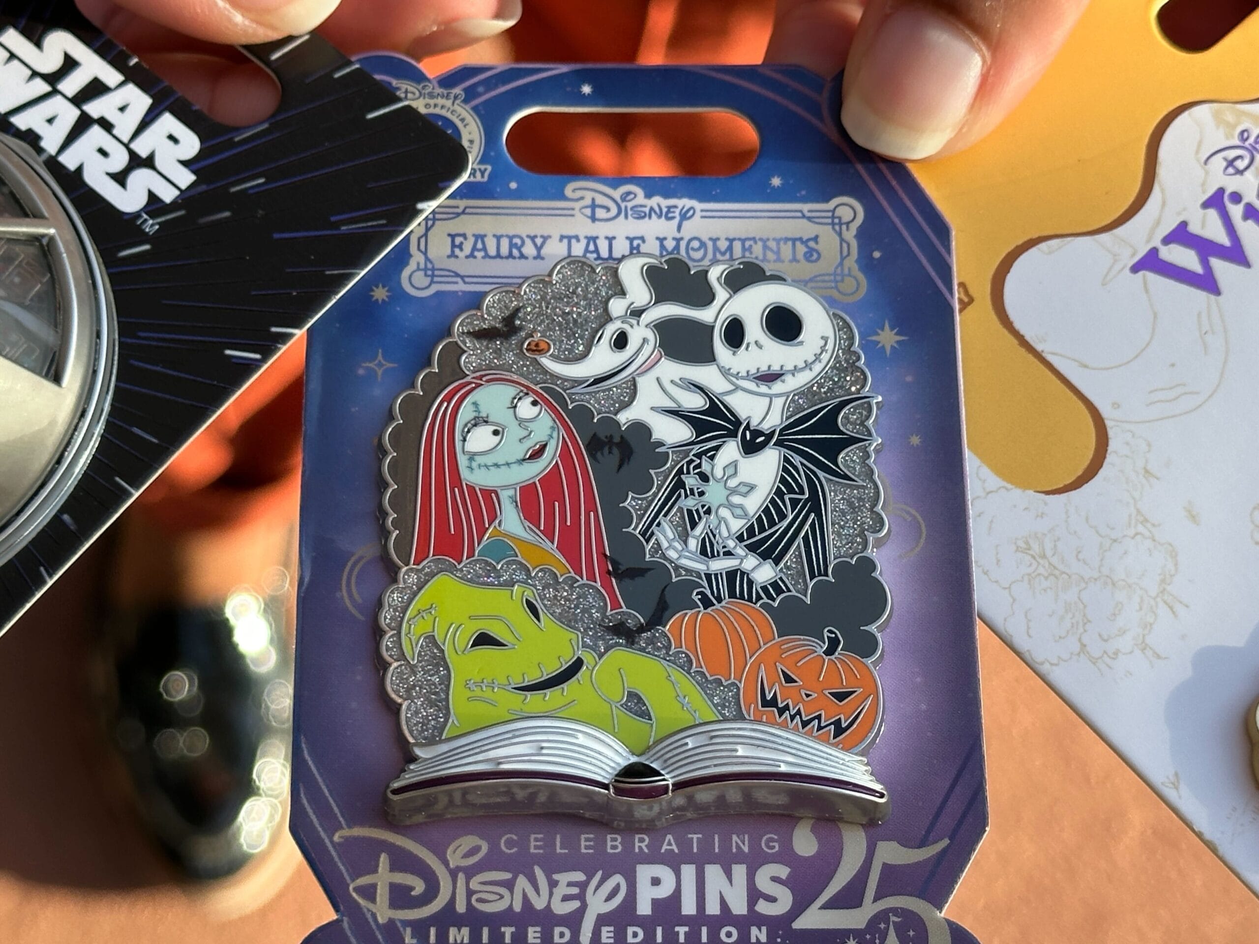 A hand holds a Nightmare Before Christmas Disney pin with Jack, Sally, Zero, and Oogie Boogie.