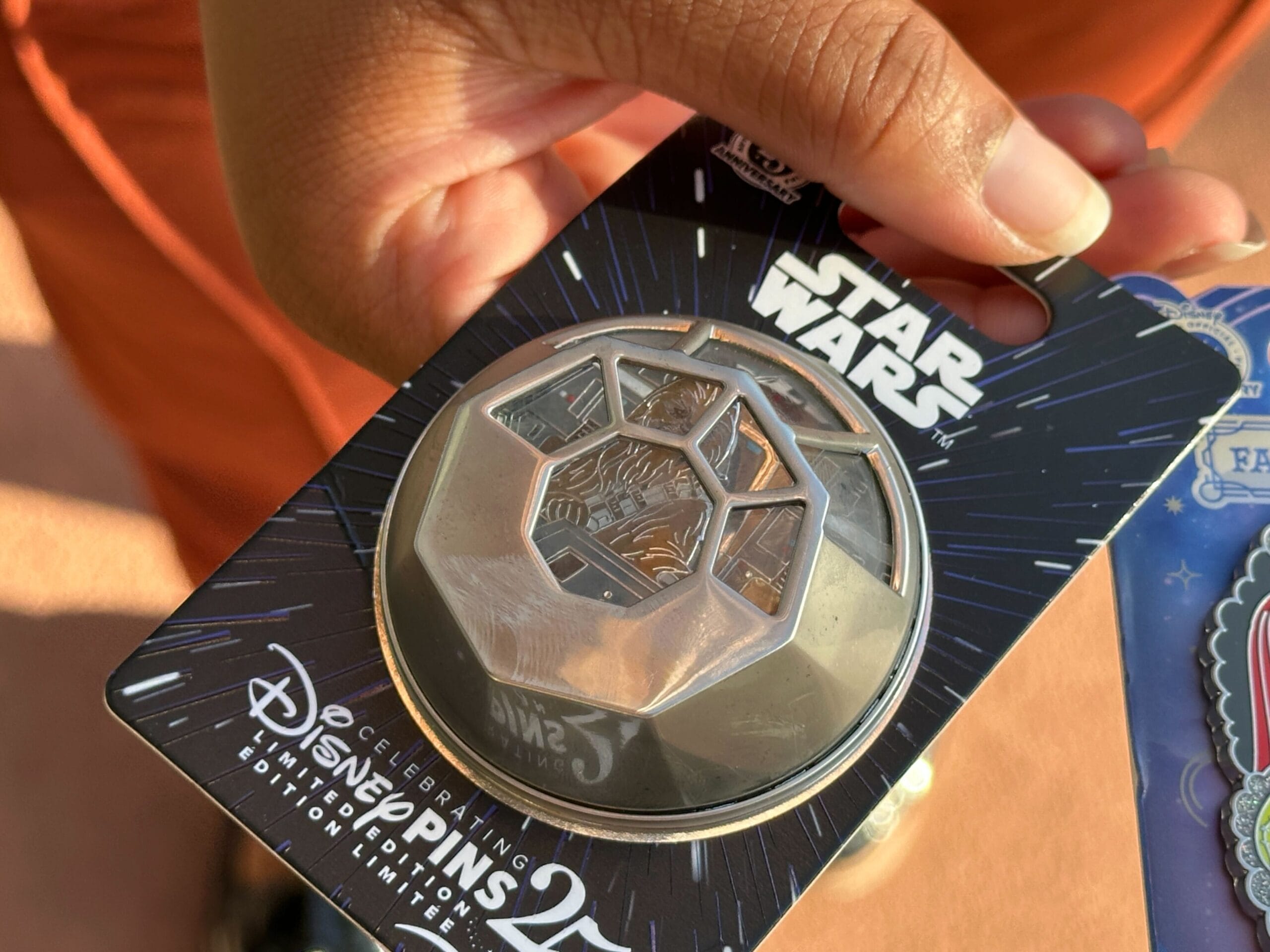 A hand holds a Star Wars or Nightmare Before Christmas pin on a Disney Pins 25th Anniversary backing card.