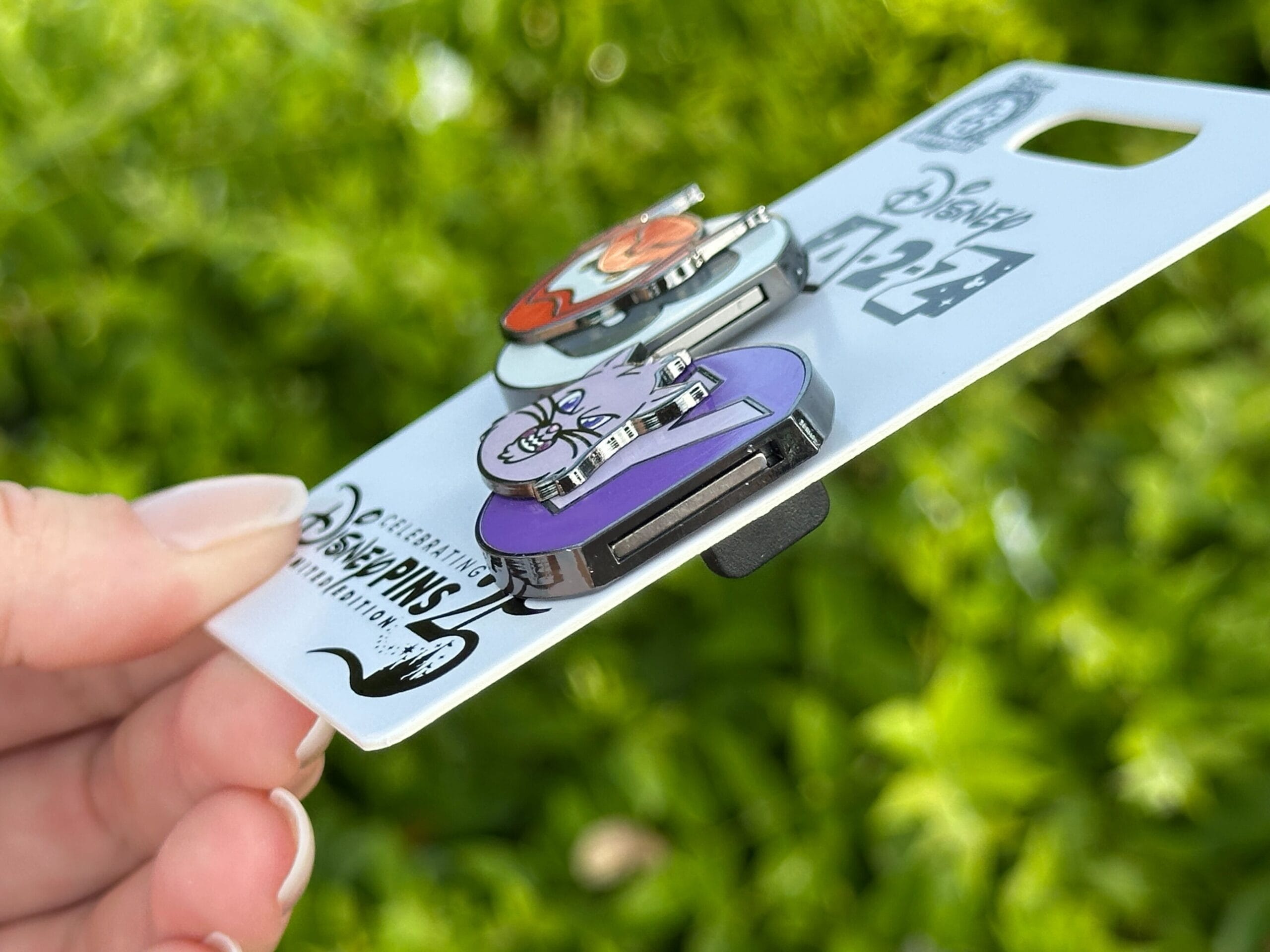 A hand displays the A-2-Z pin set for Pin Tuesday, with green foliage behind