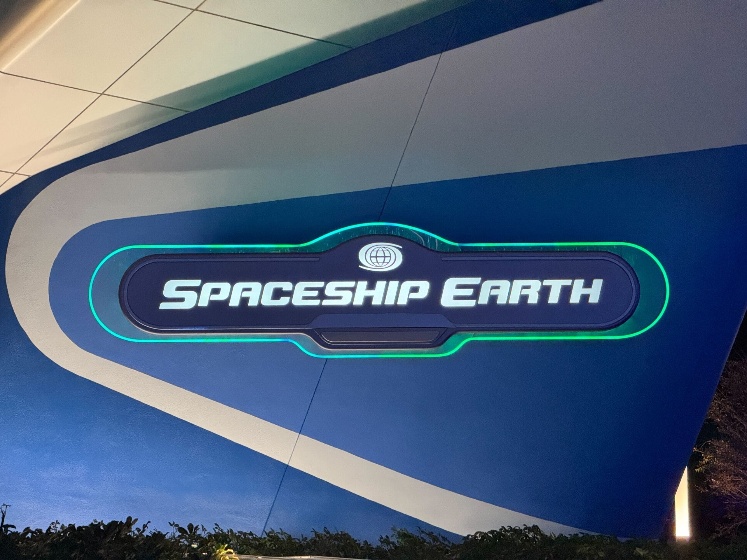 A glowing "Spaceship Earth" sign on a blue wall, with green accents and a globe icon above—evoking EPCOT at Walt Disney World.