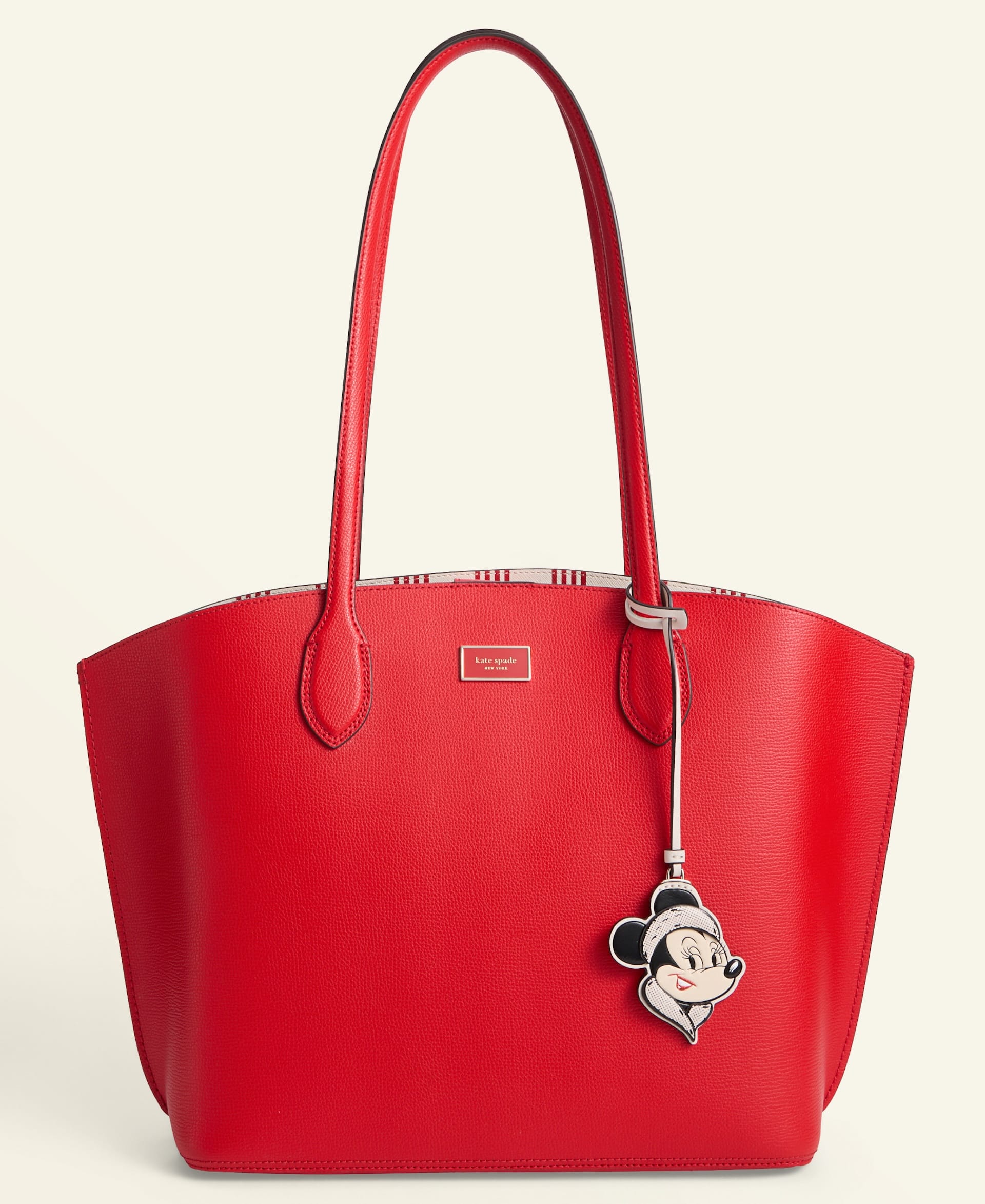 Bright red tote bag with long handles and Minnie Mouse charm, part of the Disney 2025 Holiday Collection at a Disney park.