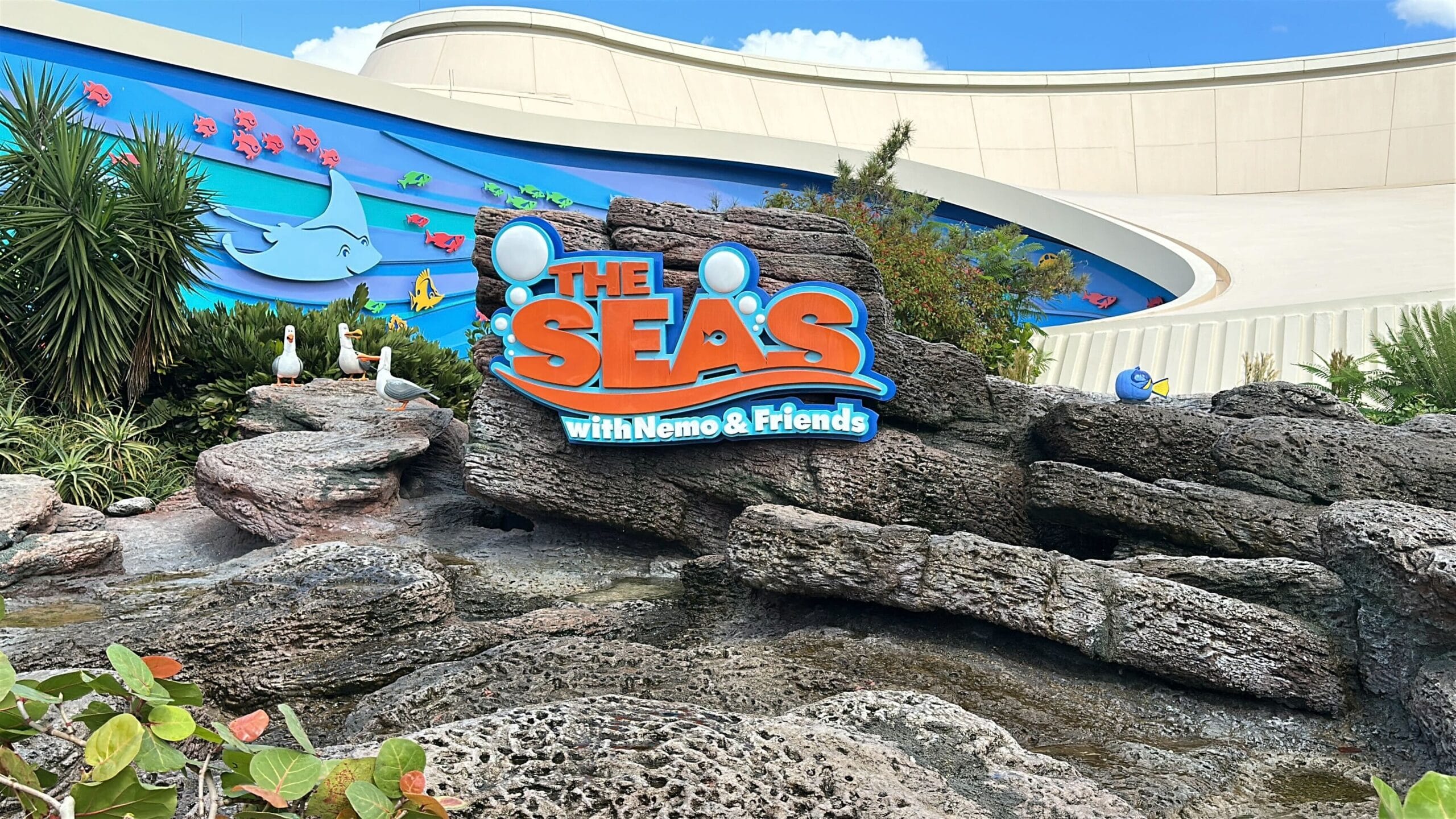 Sign for "The Seas with Nemo & Friends" at EPCOT, surrounded by rocks, greenery, playful sea characters, and a water splash effect.