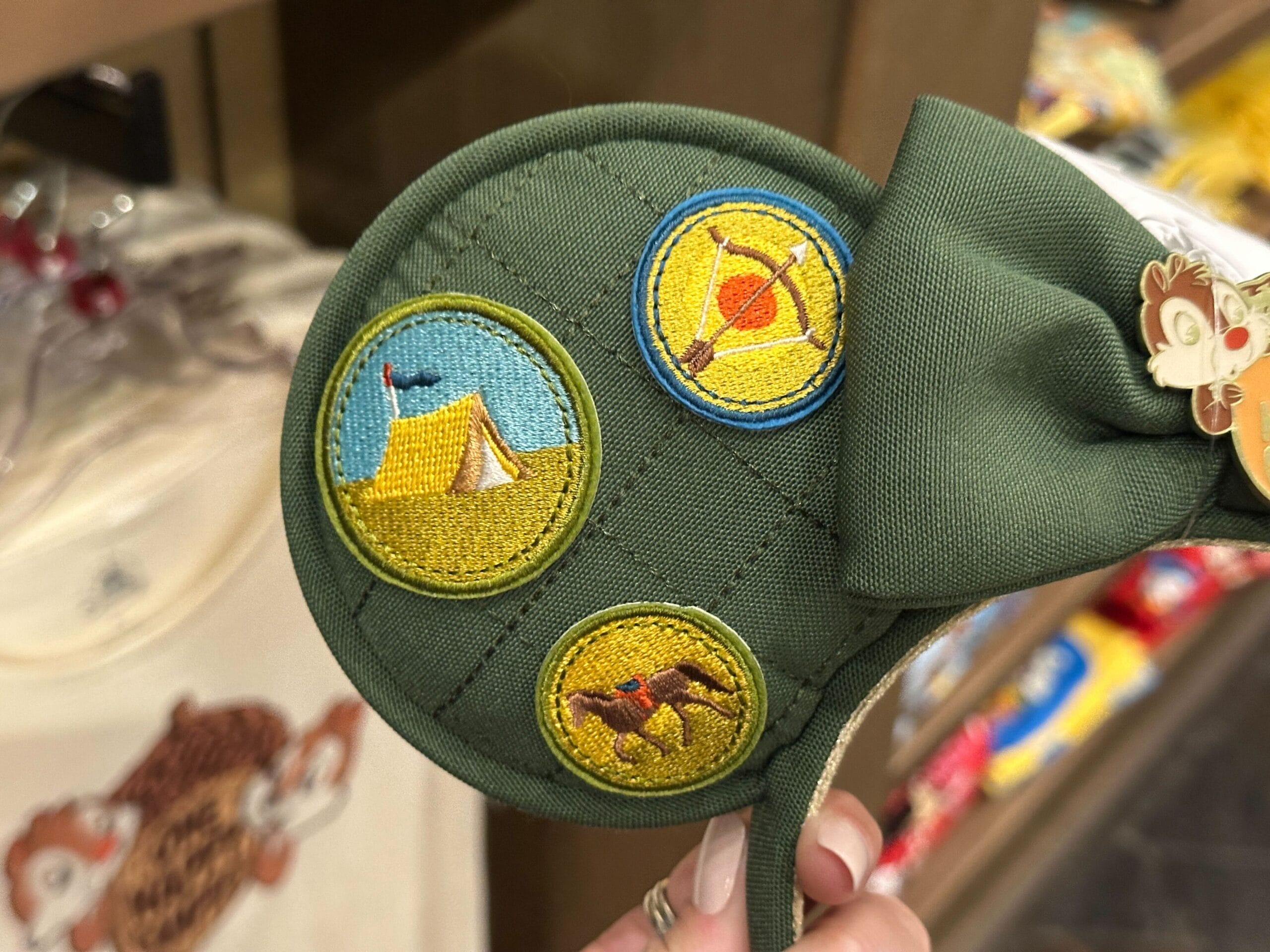 Green quilted Ear Headband with Fort Wilderness–themed camping patches: a tent, campfire, and two animals.