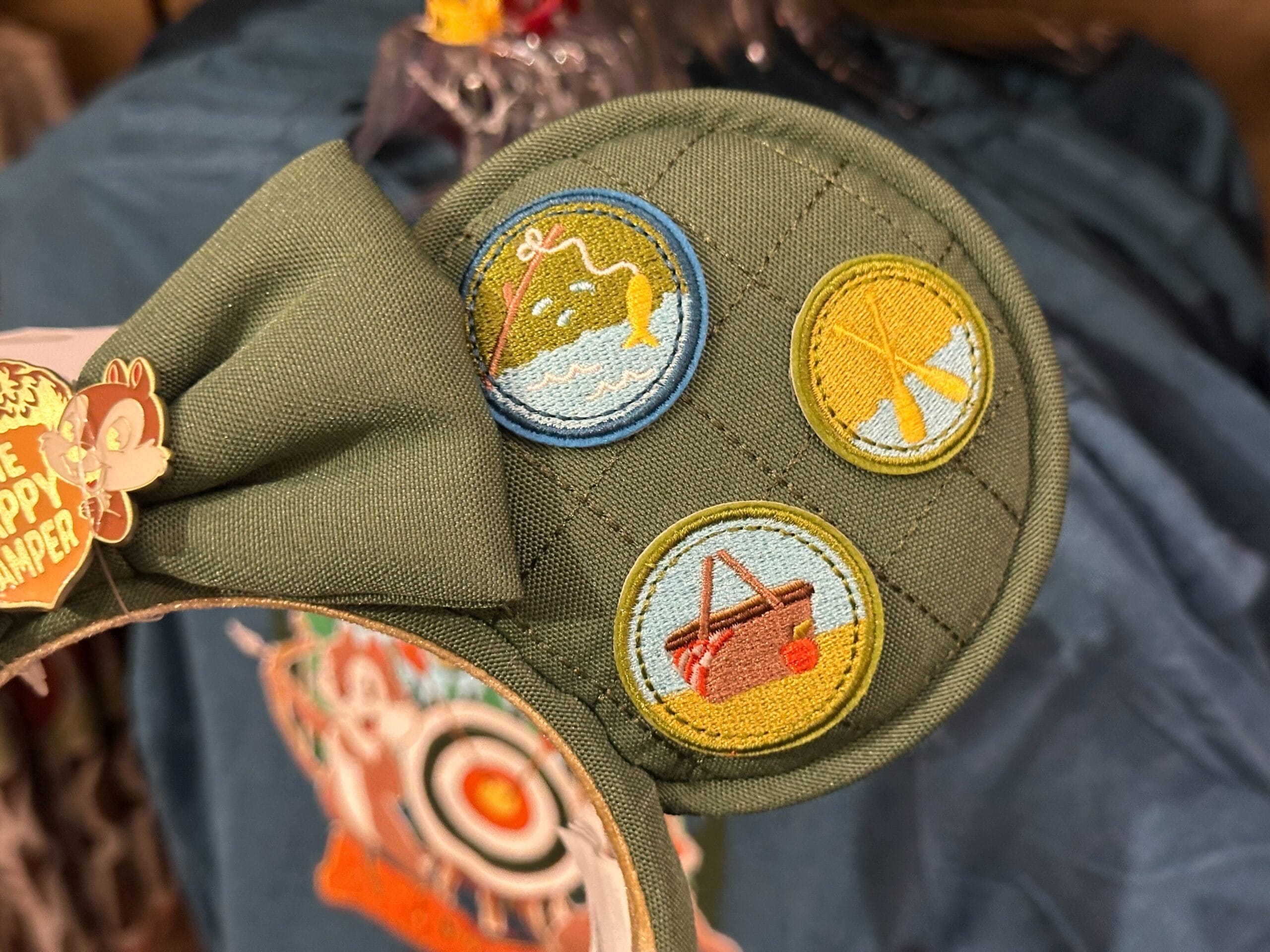 Green Fort Wilderness ear headband with three embroidered camping-themed patches: a fish, tent, and canoe on water.