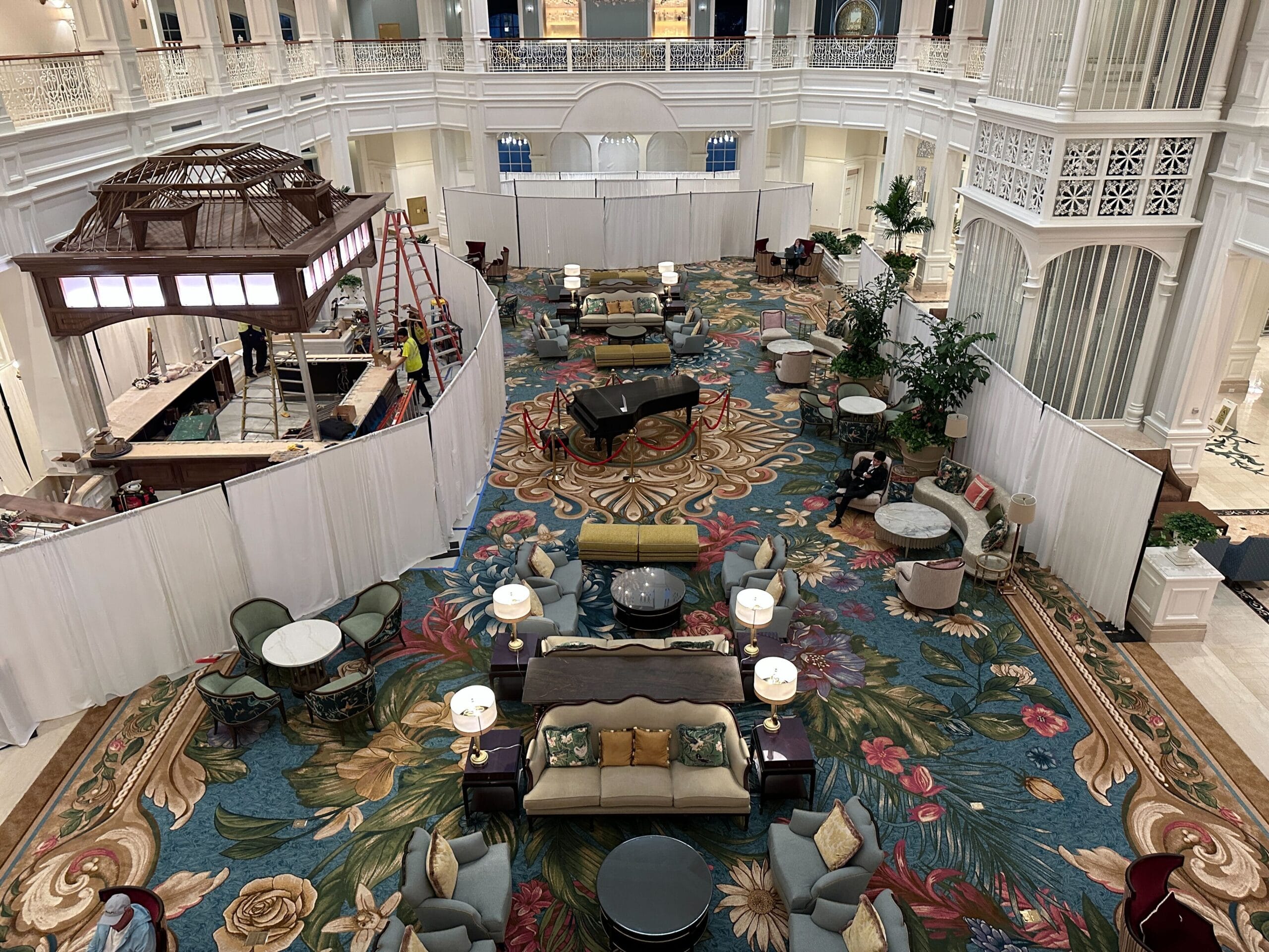 A grand Disney hotel lobby with elegant lighting, floral carpet, a grand piano, and white partitions cordoning off the space.