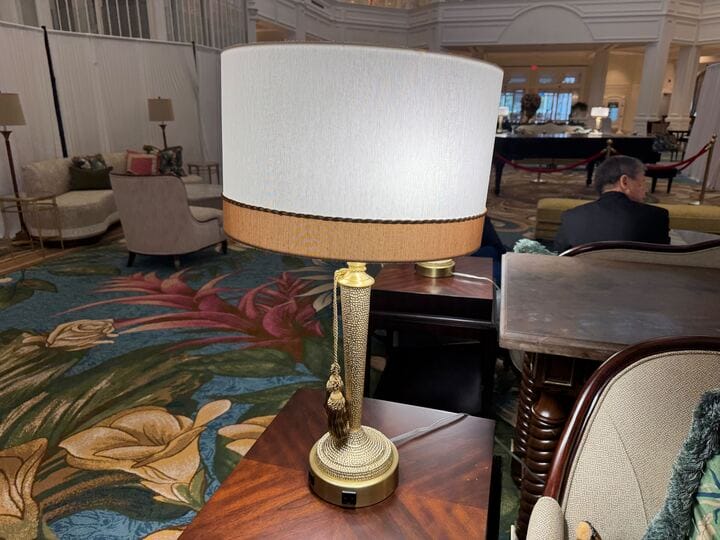 A white-shaded lamp sits on a wooden table in the floral-carpeted Grand Floridian lobby at Walt Disney World Resort.