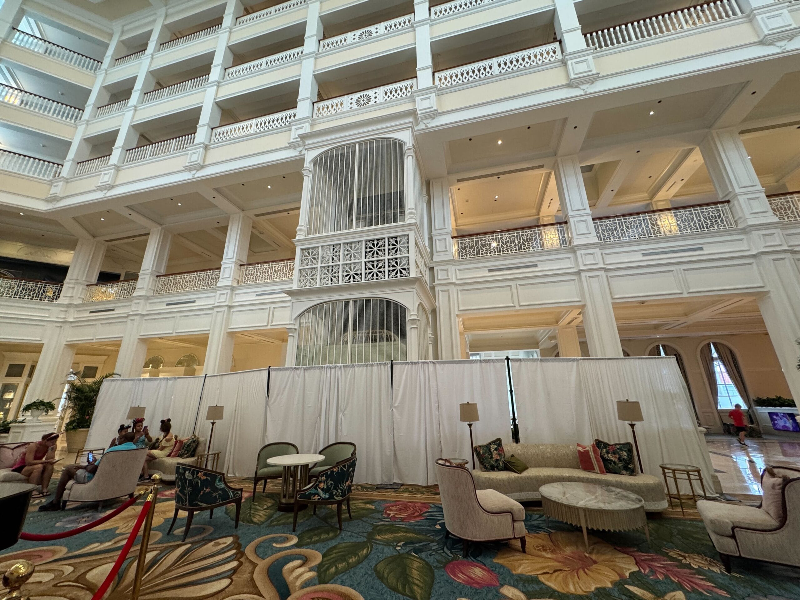 A grand hotel lobby with white walls, high ceilings, elegant seating, and curtains styled like Disney’s Grand Floridian Resort lobby.