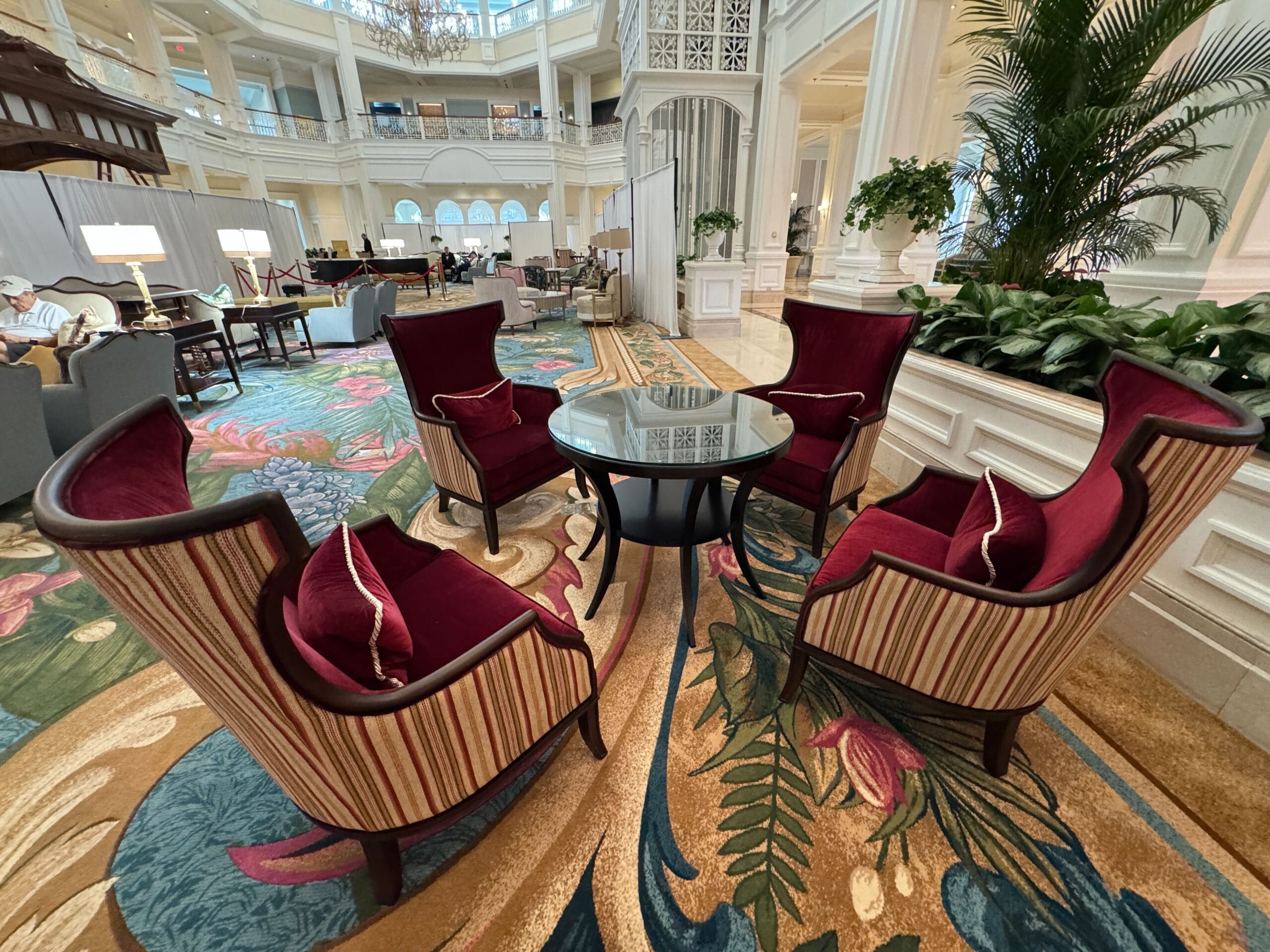 Four plush red velvet armchairs encircle a glass table in the floral-carpeted lobby of Disney’s opulent Grand Floridian Resort.