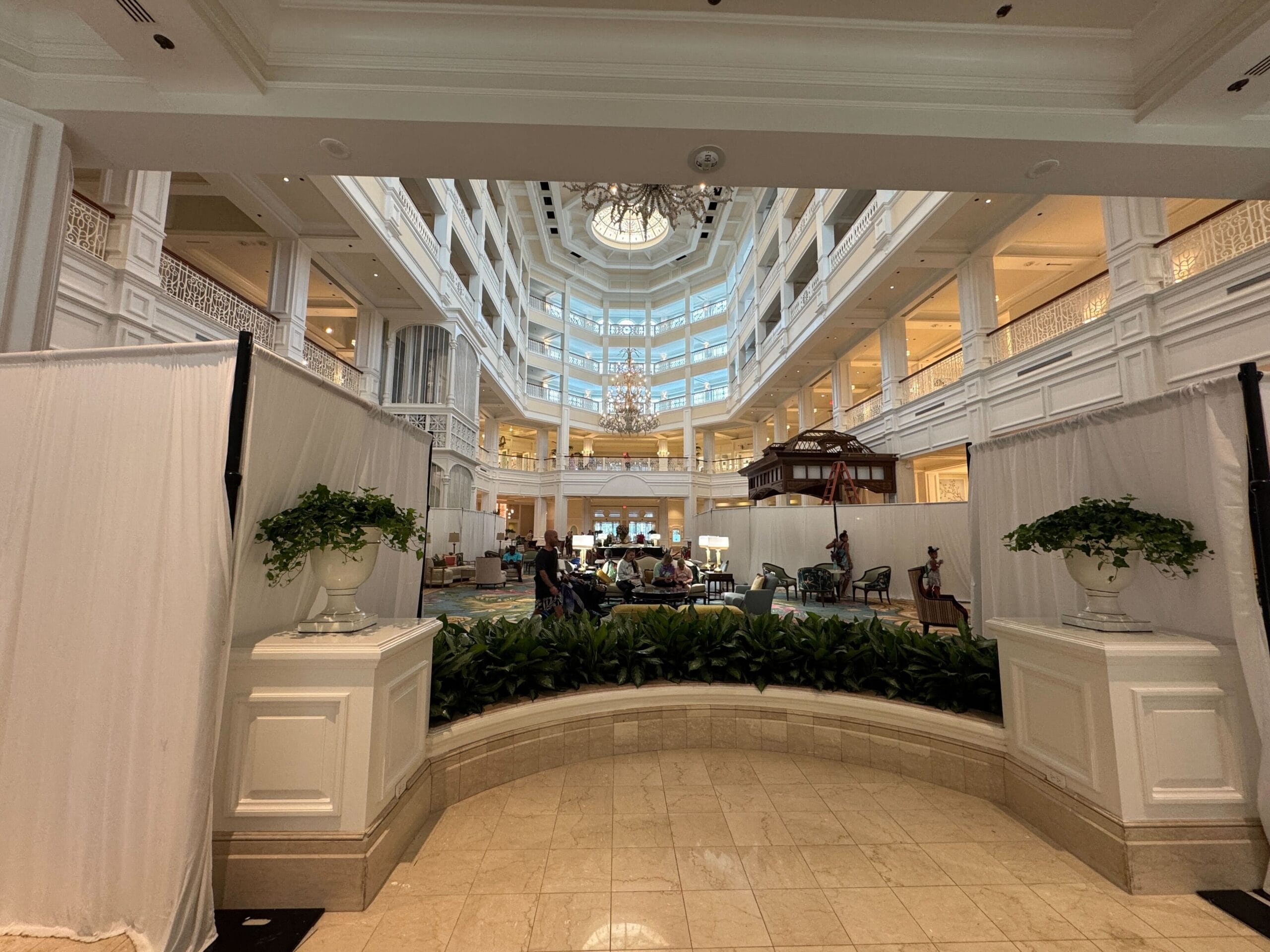 Elegant Grand Floridian lobby with classic white decor and chandeliers, plus construction barriers akin to ongoing Disney park updates.