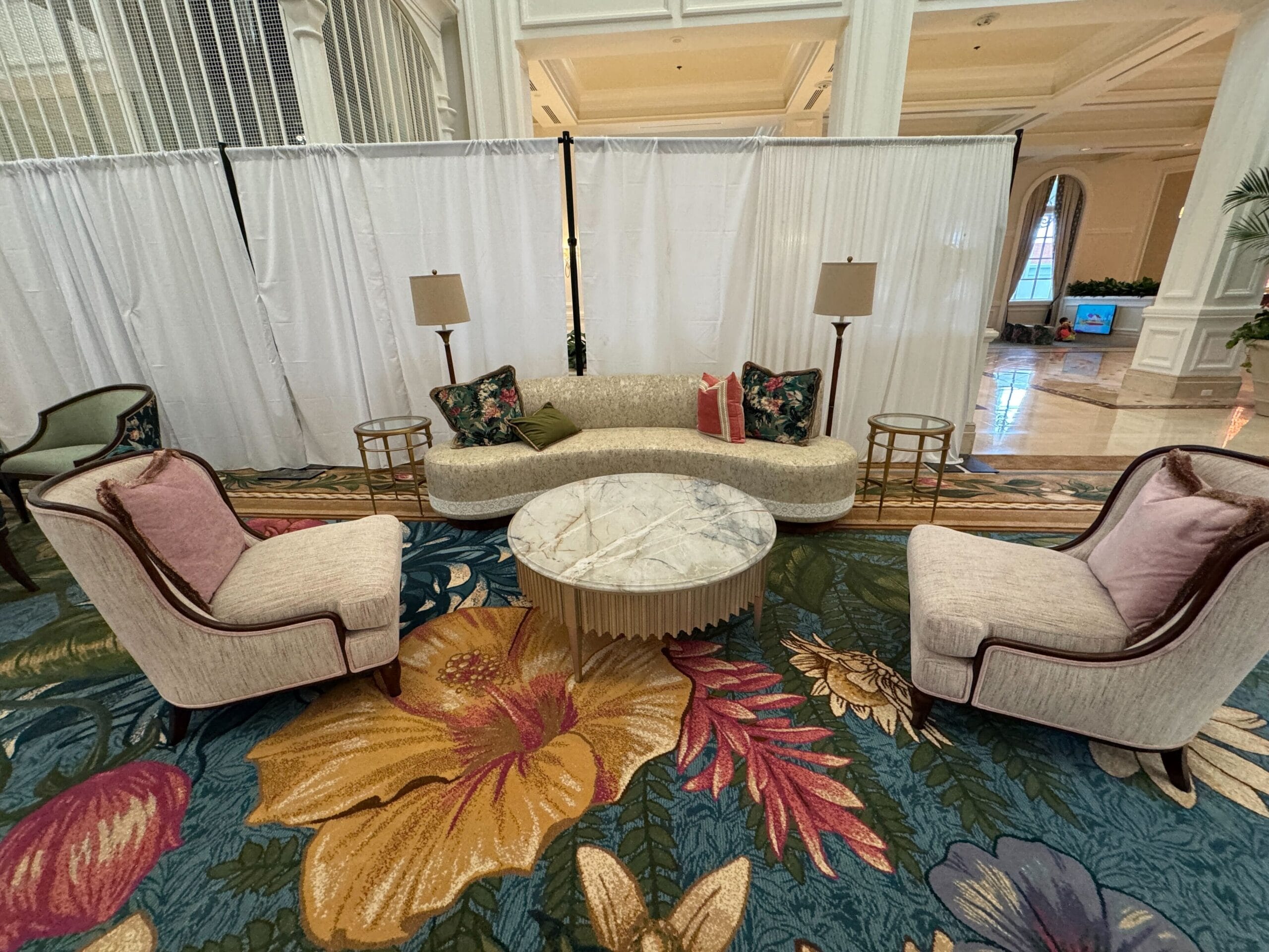 Chic lounge at Disney’s Grand Floridian, featuring a curved sofa, two armchairs, and ornate floral carpet—no castle in view.