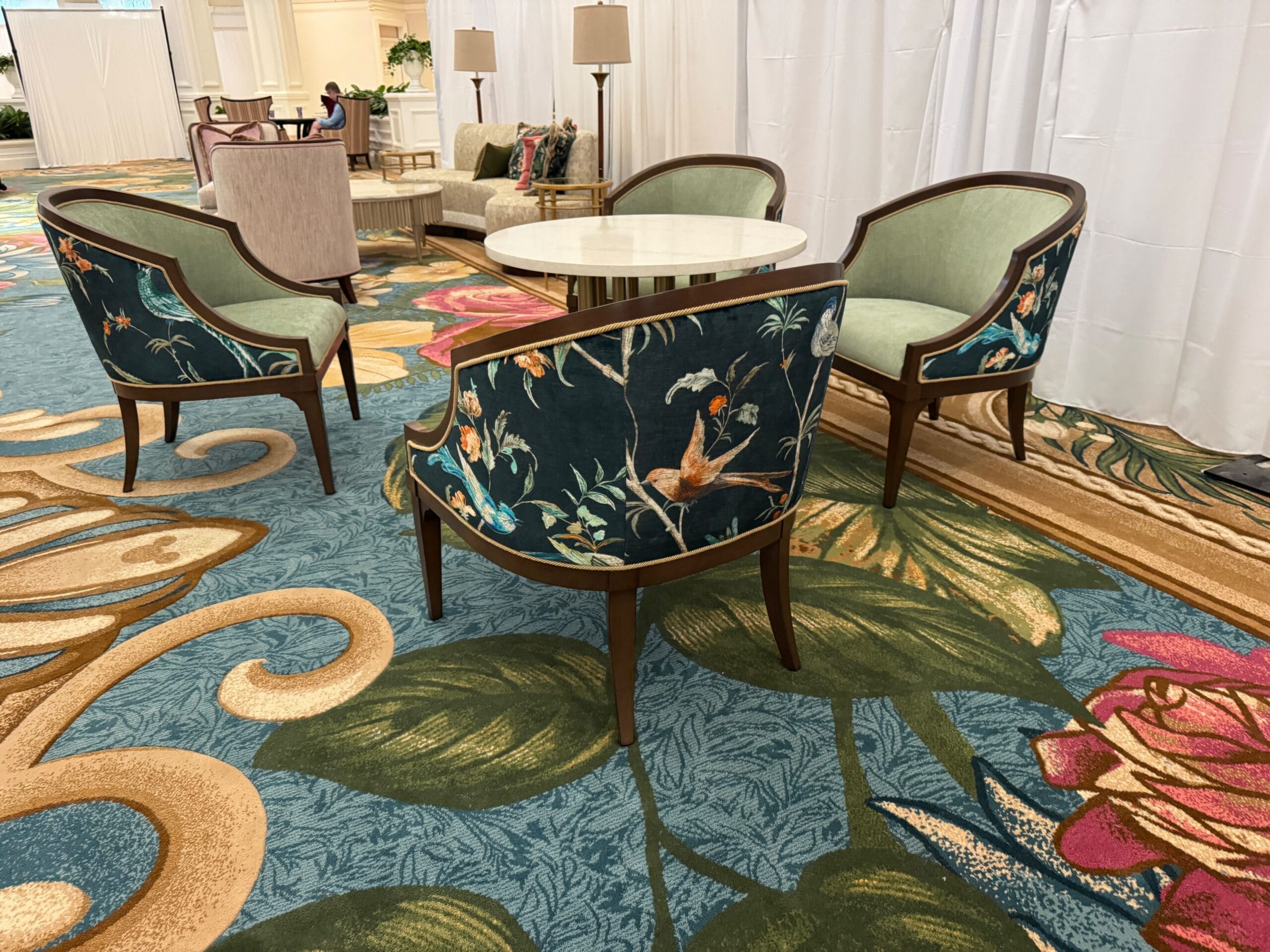 A round table with four floral-upholstered chairs rests on a patterned carpet in Disney’s Grand Floridian, evoking classic Disney elegance.