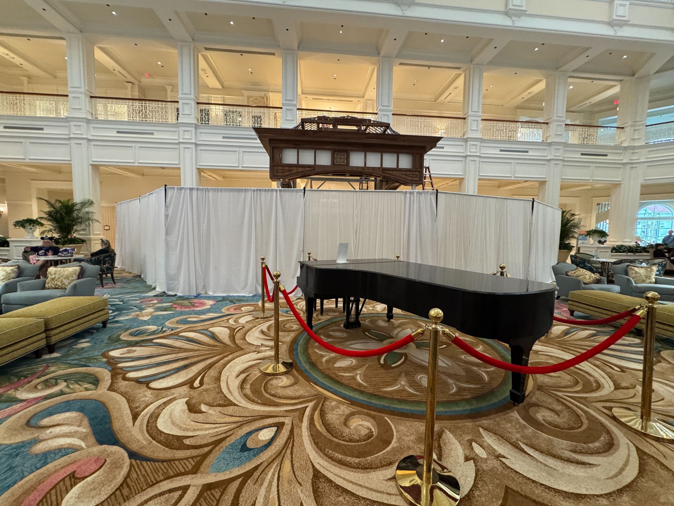 A grand piano sits behind red ropes in Disney’s Grand Floridian Resort lobby; white curtains cover space behind, no castle in view.