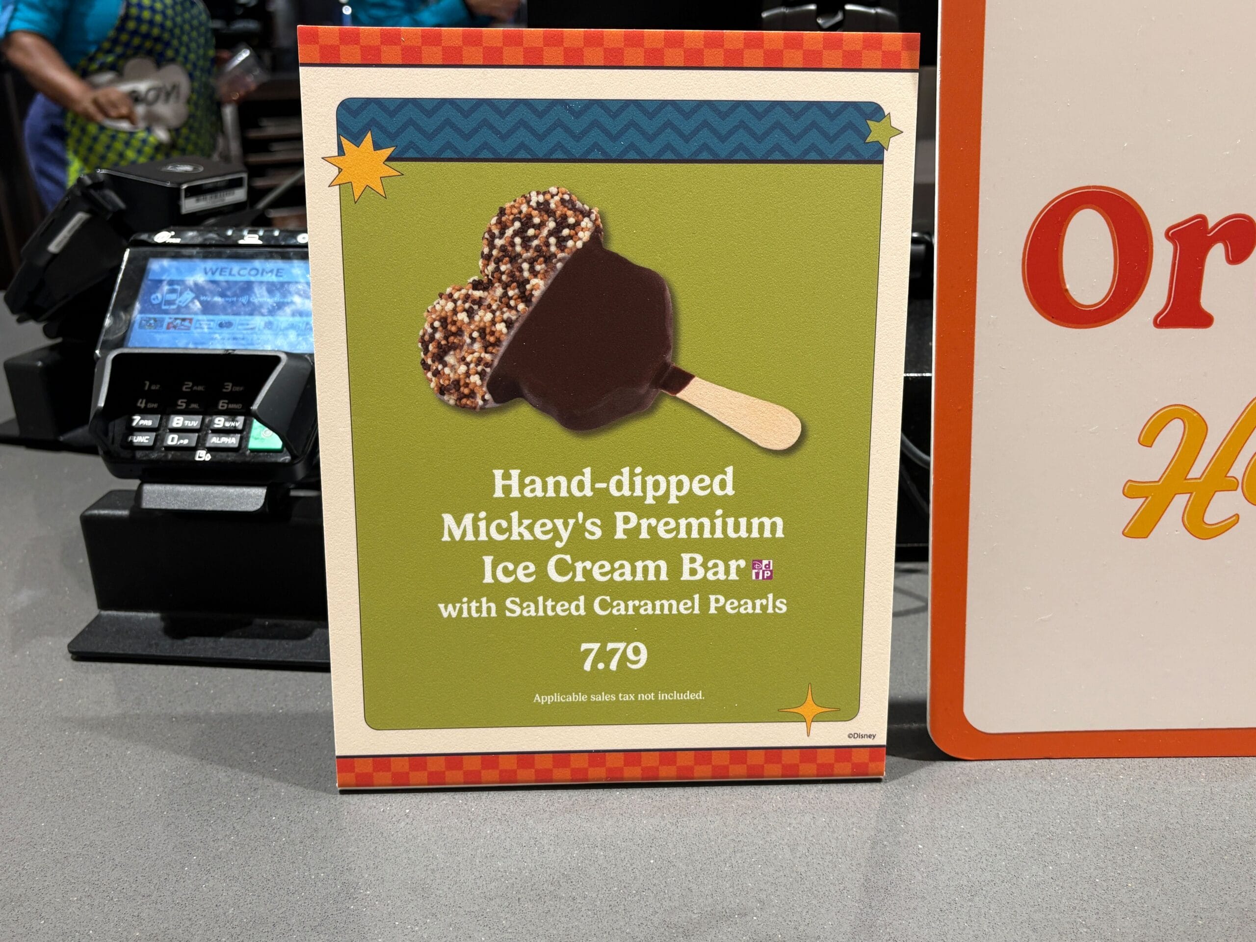 A Disney park sign promotes a hand-dipped Mickey’s Premium Ice Cream Bar with salted caramel pearls for $7.79.