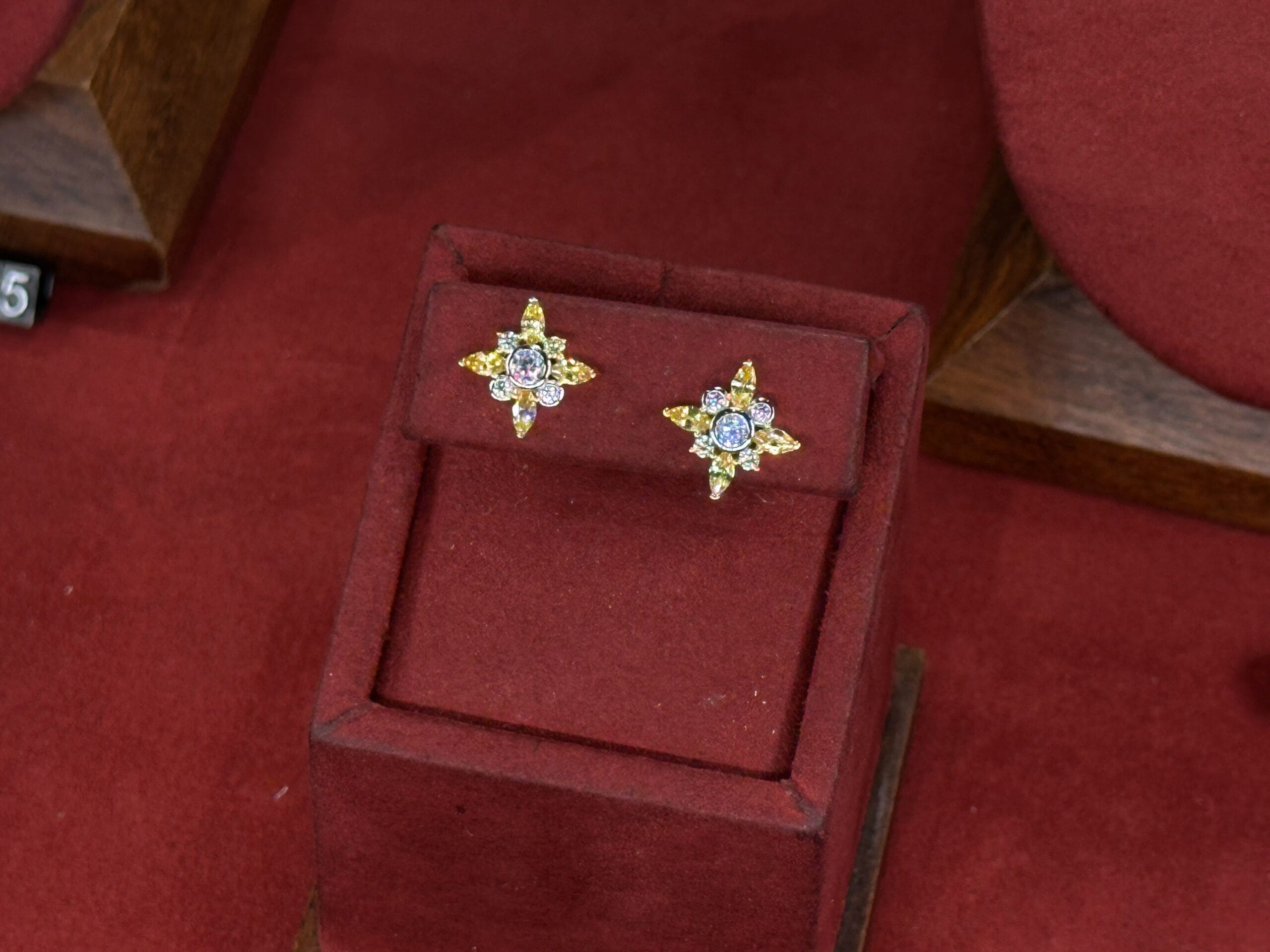 A pair of star-shaped gold earrings with gemstone centers rest on a red velvet stand, reminiscent of Main Street jewelry shops in Disney Parks.