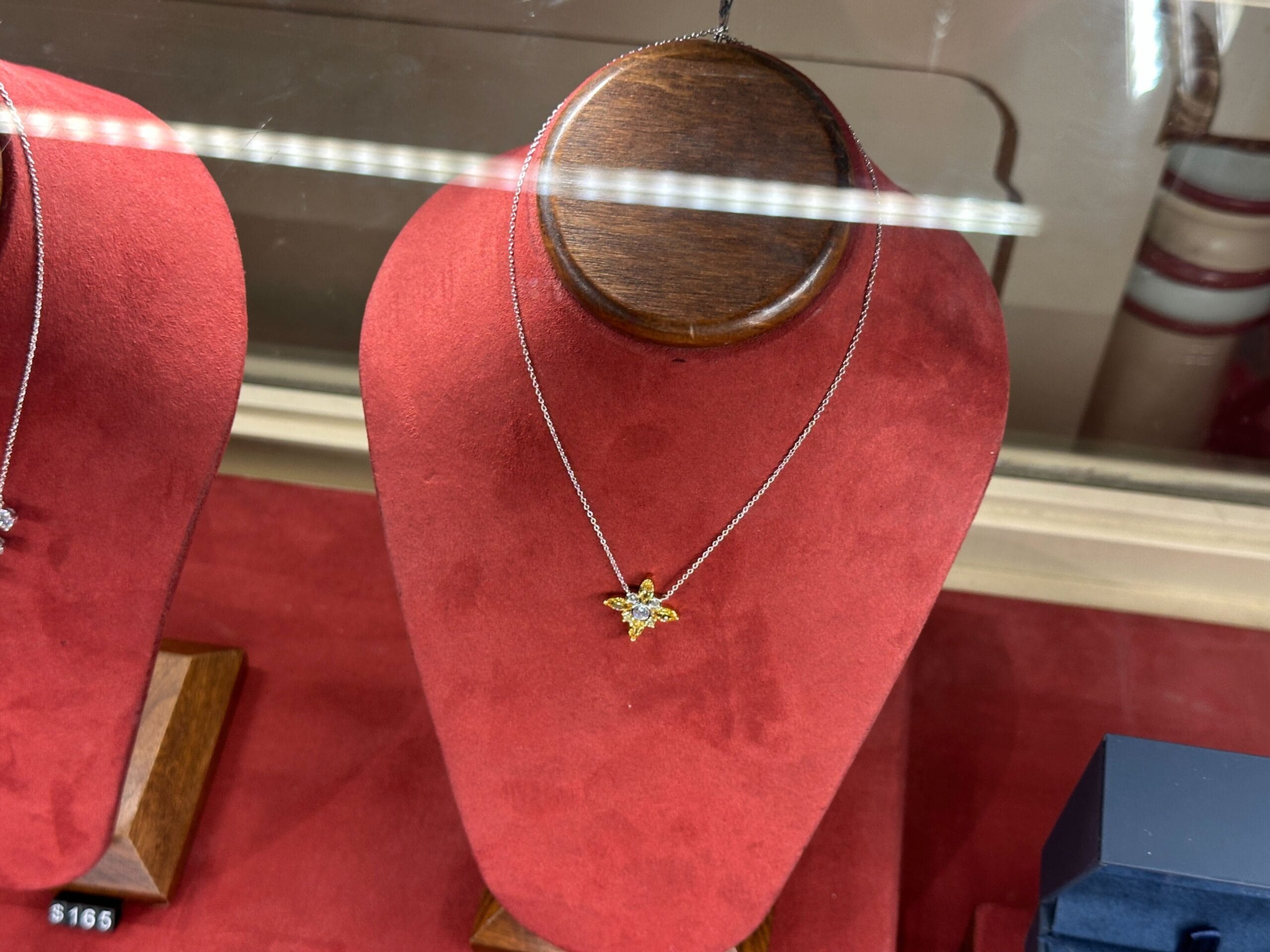 Gold and diamond star-shaped pendant necklace on a red velvet stand in a glass case, like jewelry seen in Main Street shops at Disneyland.