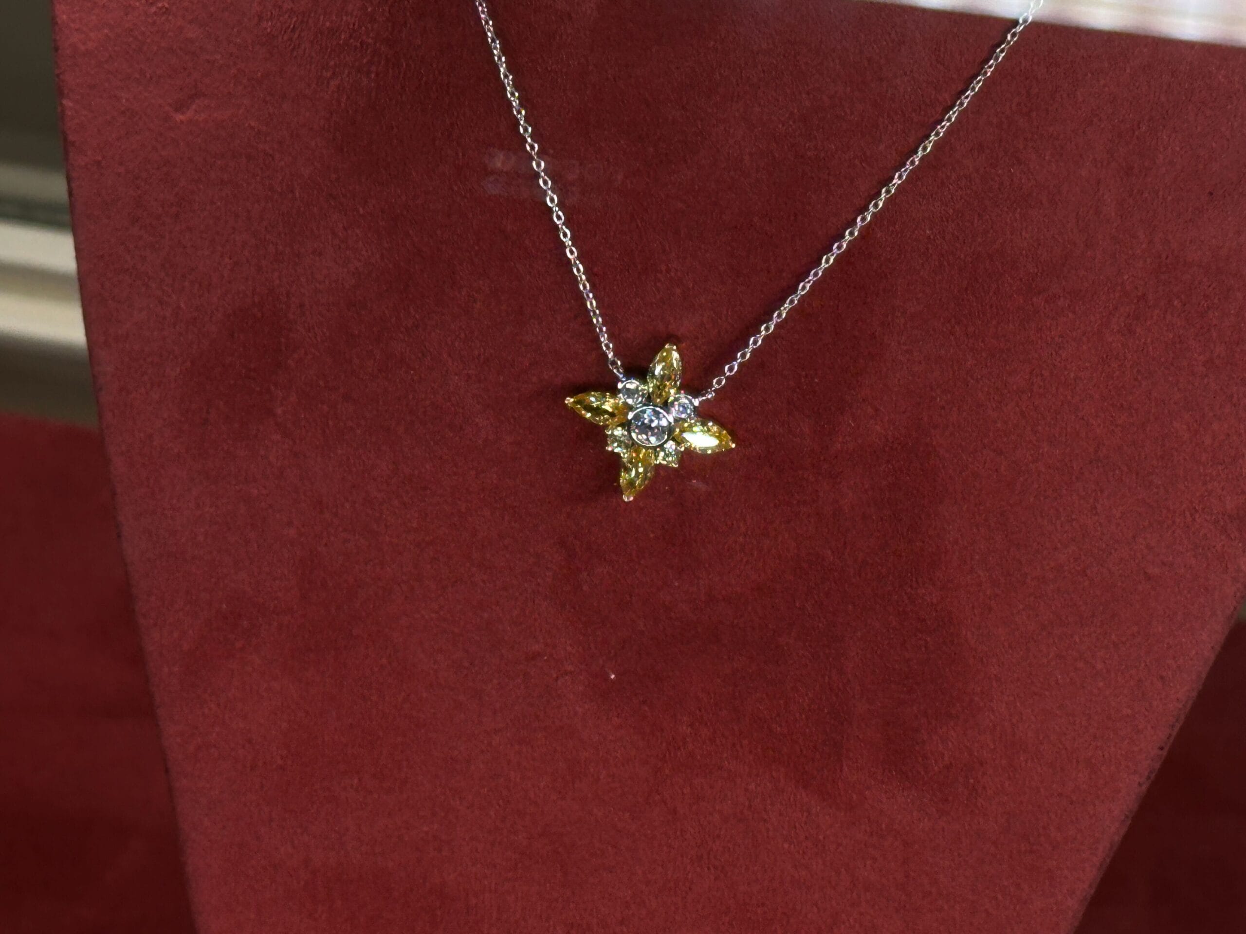 A silver necklace with a yellow and white flower-shaped pendant on red velvet, reminiscent of jewelry found in Disney Parks gift shops.