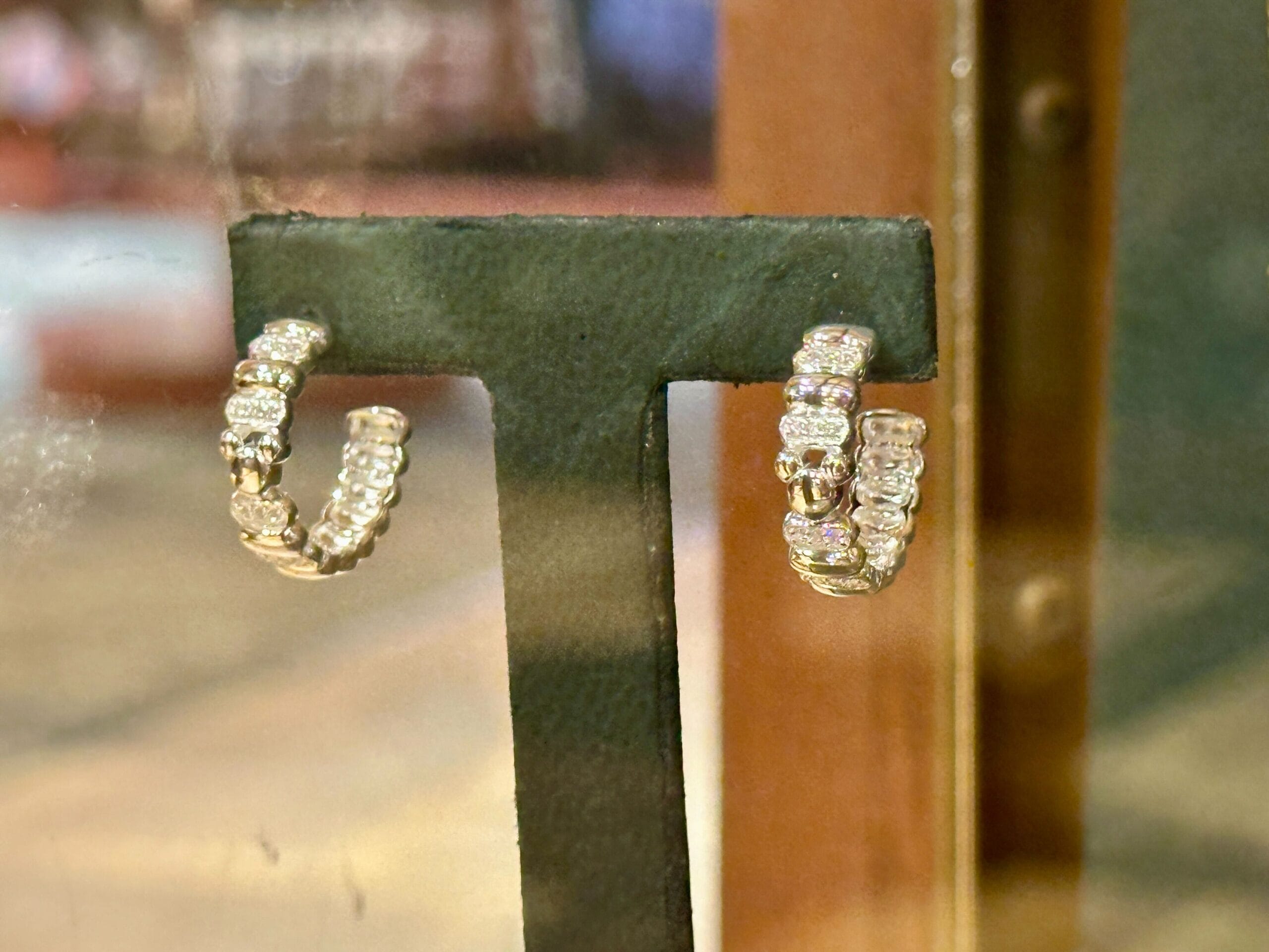 A pair of gold hoop earrings encrusted with diamonds sparkle behind glass, reminiscent of regal Disney castle treasures.