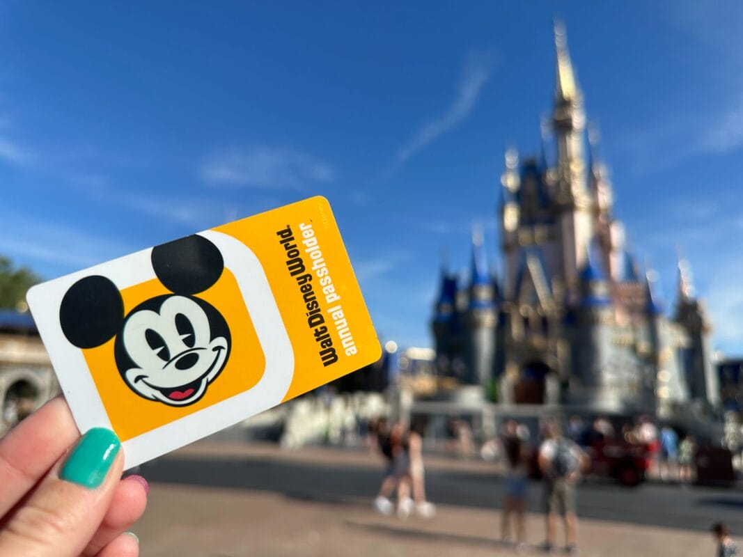 A hand shows a Walt Disney World annual passholder card with Cinderella Castle in the background./