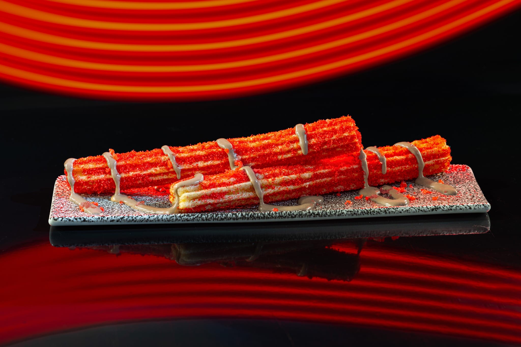 Three vibrant red Astro Fizz churros with white drizzle on a plate, in front of Cool Ship’s vivid Disney Tomorrowland backdrop.