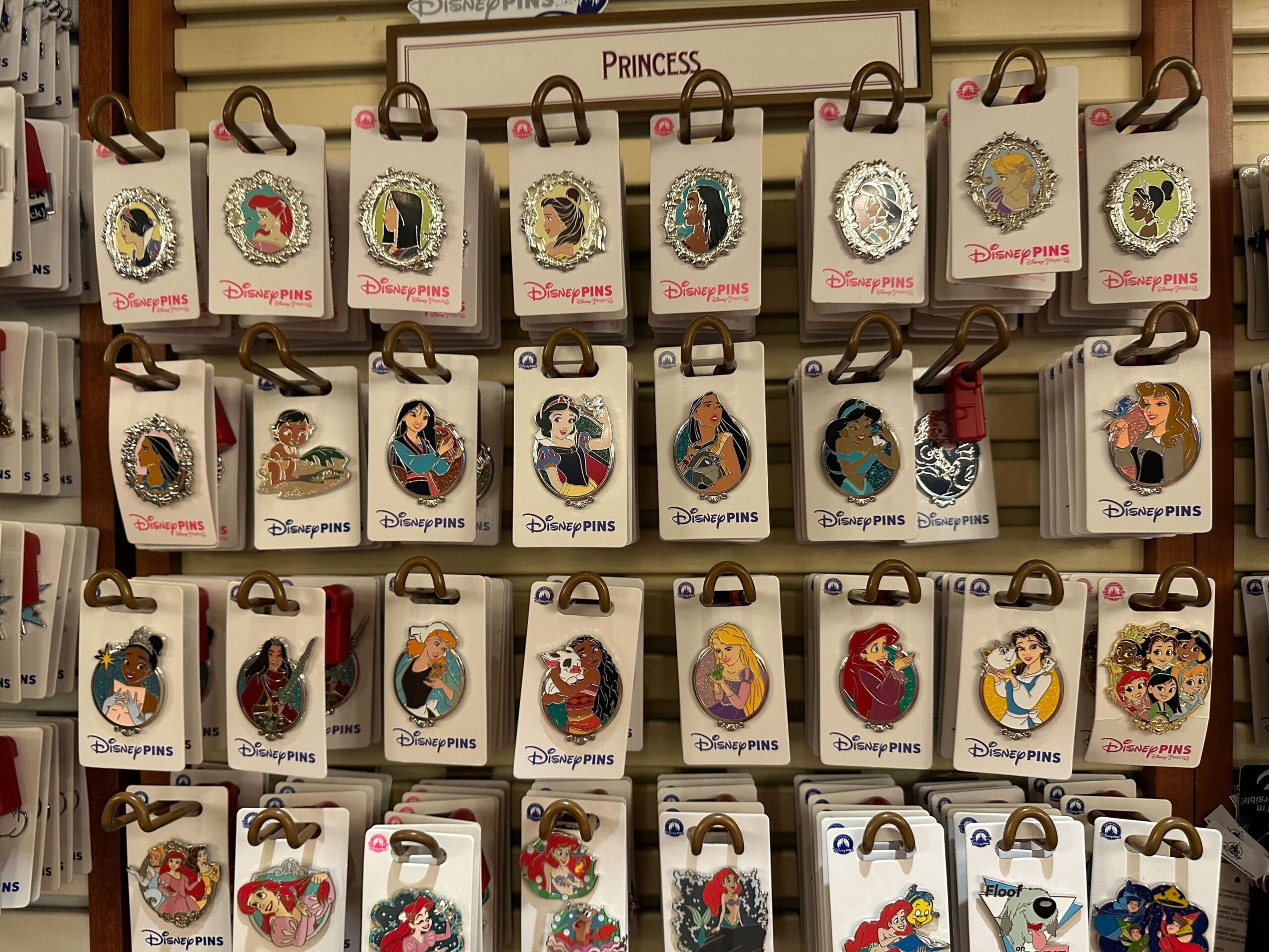 Disney Princess and Sidekick pins on a store rack at a Disney Park, featuring vibrant designs inspired by global park magic.
