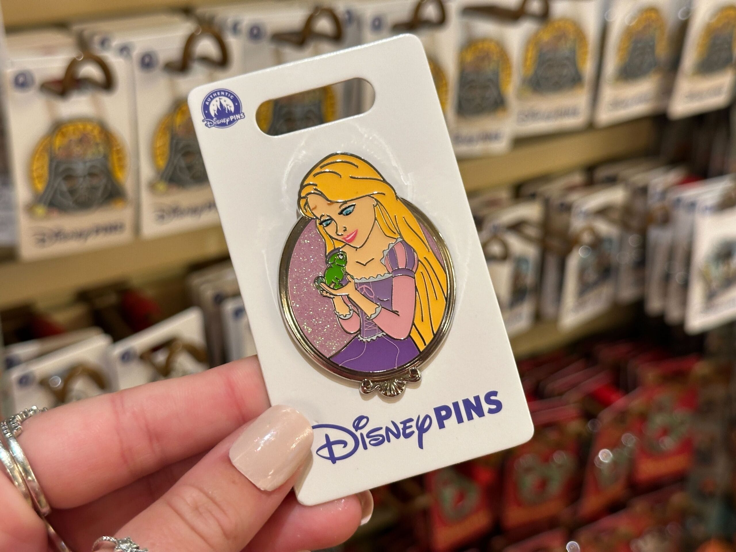 A hand holds a Rapunzel and Pascal Disney Princess Sidekicks Pin on a card at Walt Disney World, not far from Cinderella Castle.