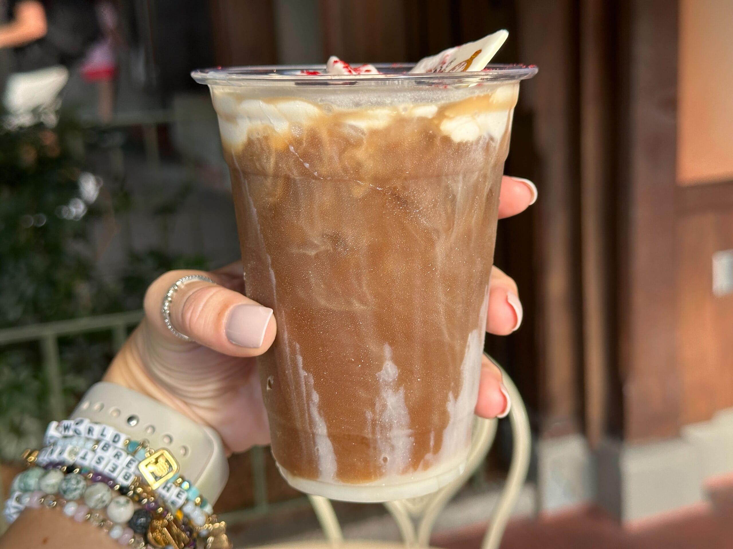 A hand holds a White Rabbit Cold Brew at Magic Kingdom, featuring iced coffee, cream, whipped topping, and a straw nearby Cinderella Castle.