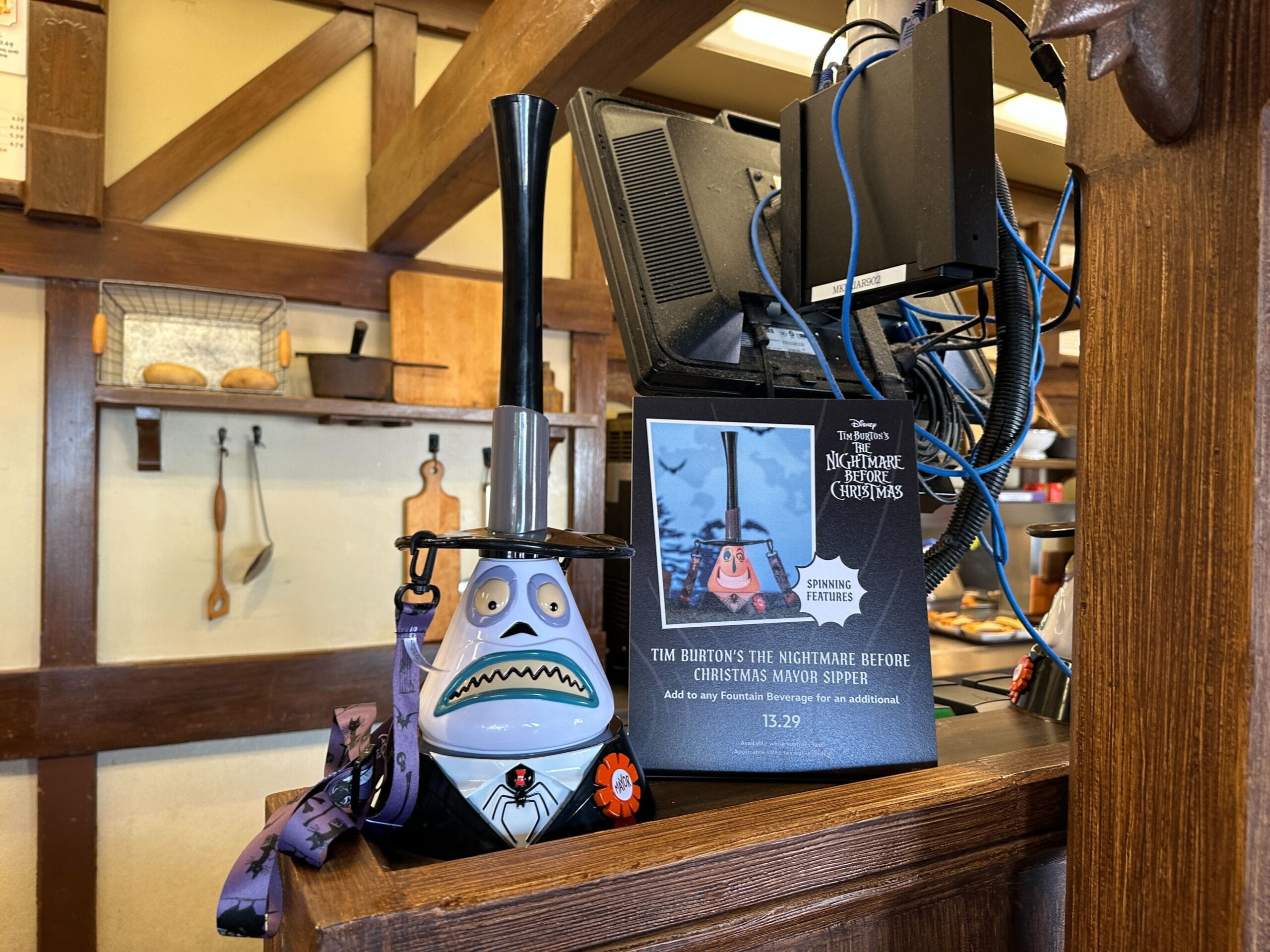 An Exclusive Nightmare Before Christmas Sipper mug with a straw sits by a sign on a wooden counter.