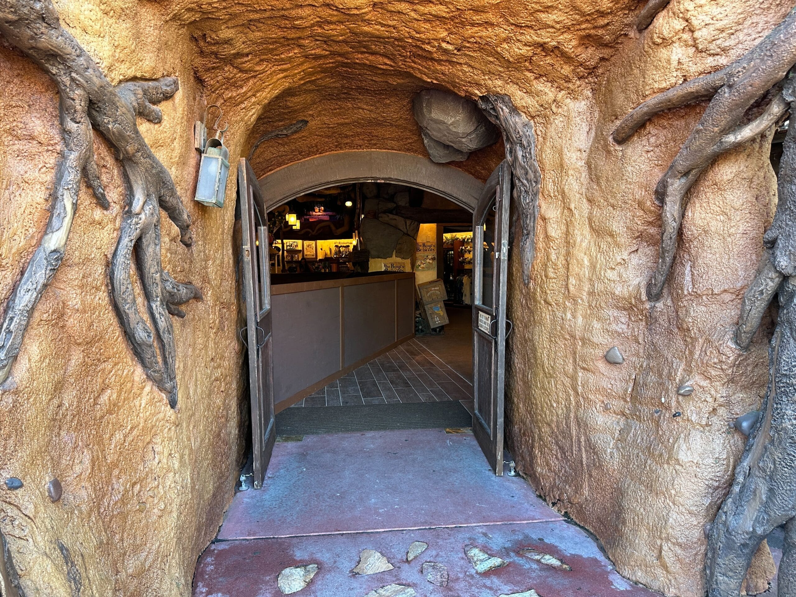 Double doors open in a tree root tunnel entrance, leading into Disney World's cozy, warmly lit Critter Co-Op—no castle in view.