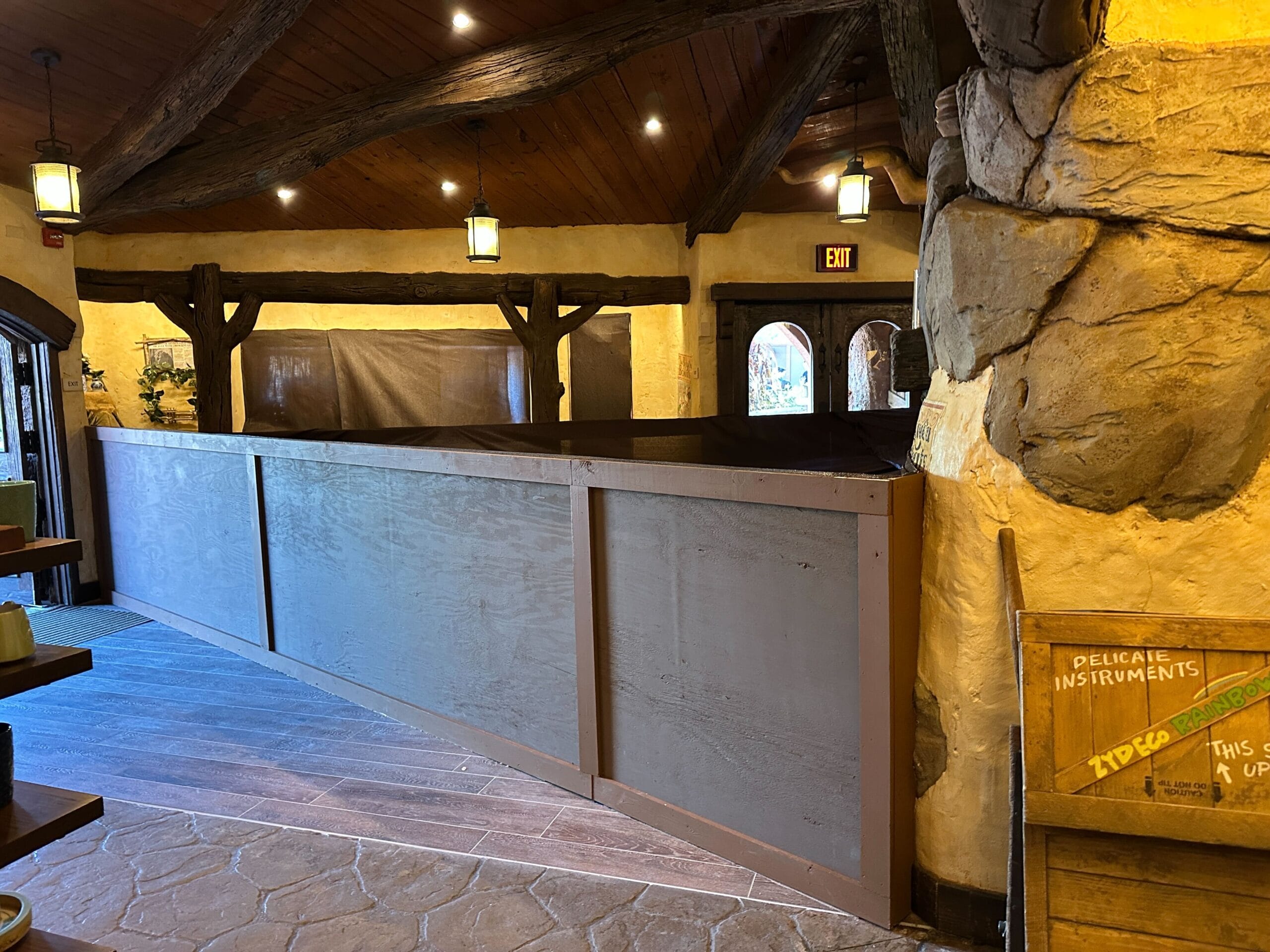 A wooden construction wall blocks part of Critter Co-Op during floor work in a rustic, stone-walled space at Disneyland.