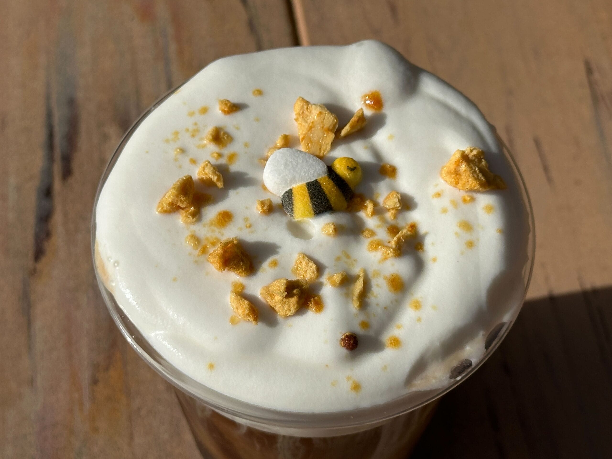 A Honey-Lavender Cold Brew from a Disney park, piled with whipped cream, crunchy flakes, and a cute candy bee on top.