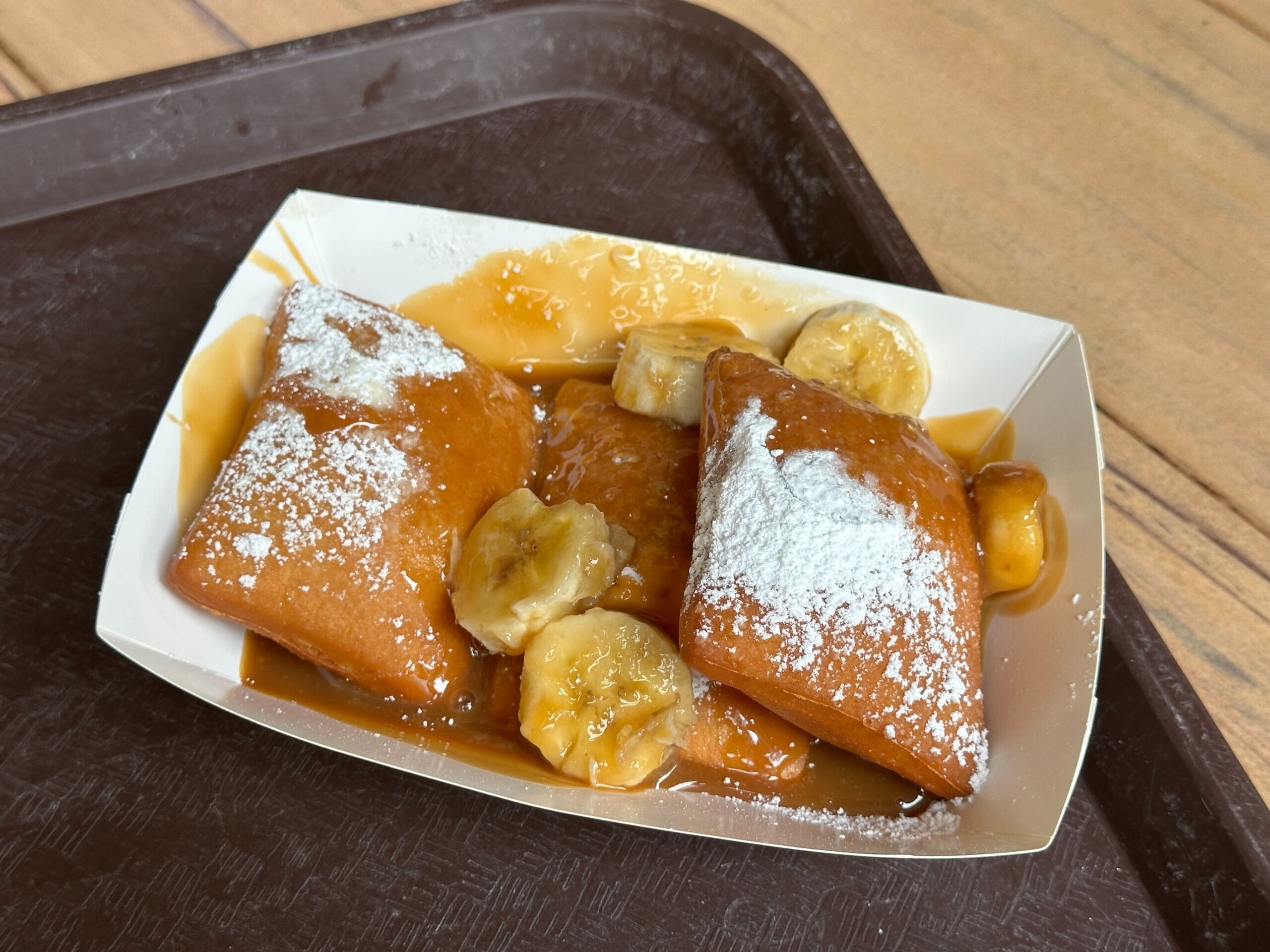 Beignets with powdered sugar, bananas, and caramel sauce from Golden Oak Outpost at Magic Kingdom near Cinderella Castle.