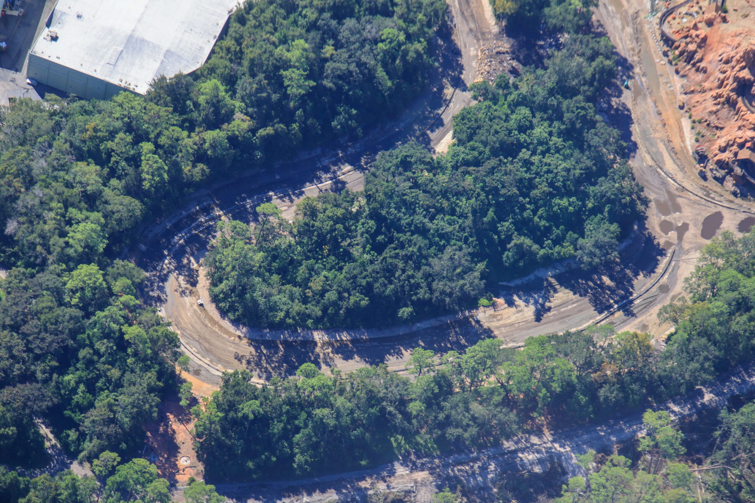 Aerial view of a winding dirt road through dense trees, with a building and Disneyland’s Rivers of America visible in the top left.