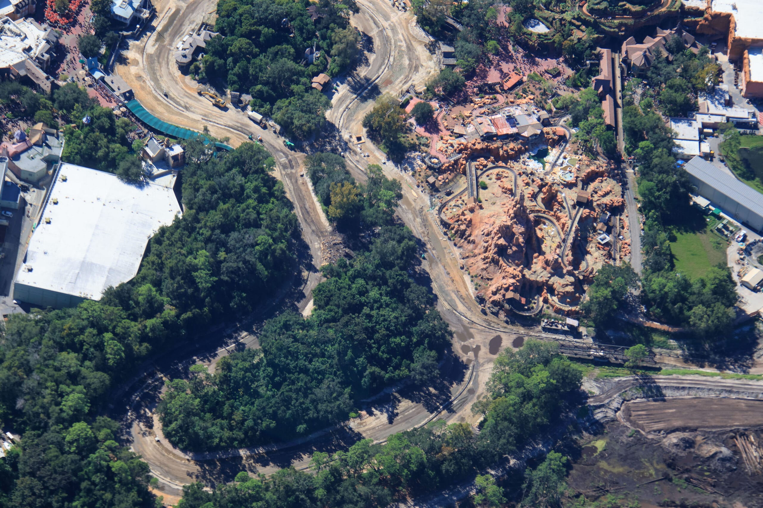 Aerial view of a Disney park construction shows winding dirt paths, trees, and the Rivers of America, reminiscent of Disneyland.