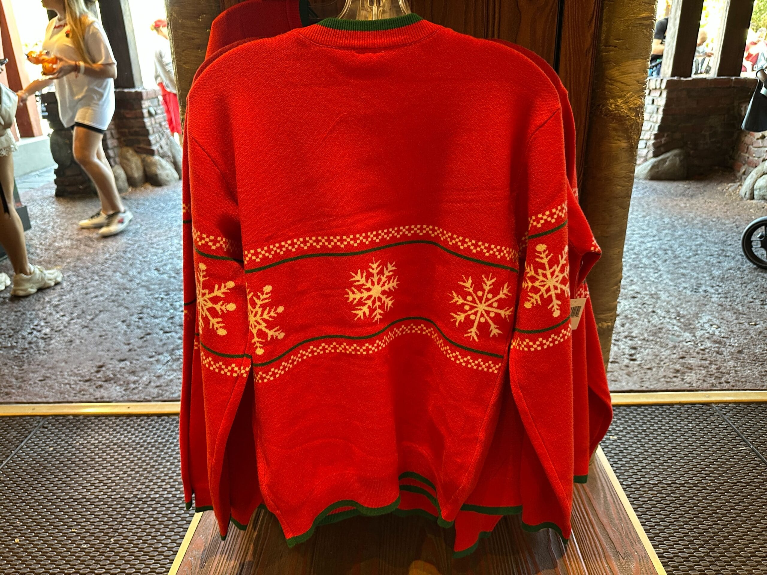 Red holiday sweater with white snowflake and geometric patterns on a store rack at a Disney park.