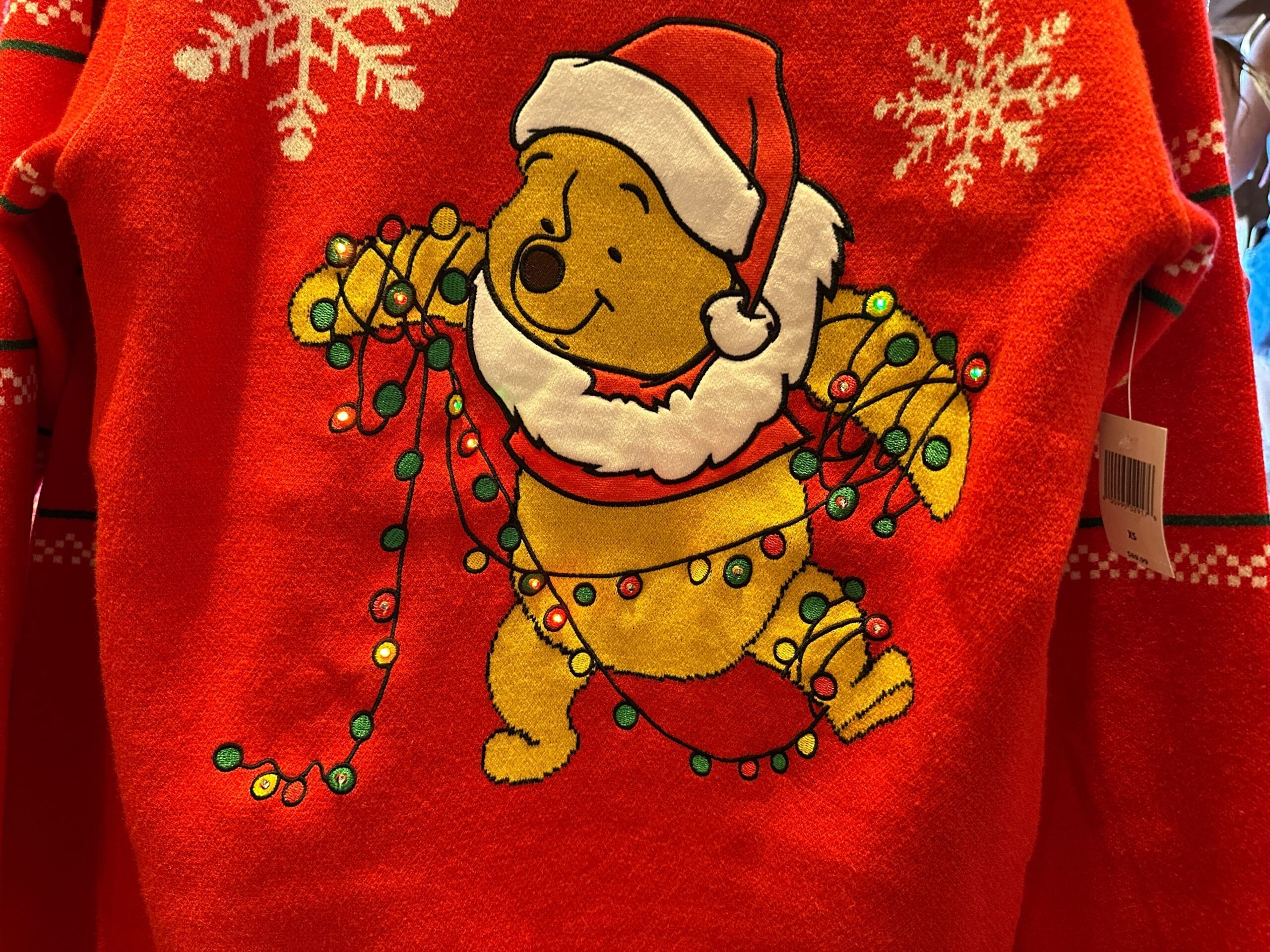 Winnie the Pooh in a Santa hat tangled in holiday lights on a festive sweater with white snowflakes, perfect for Disney Parks.