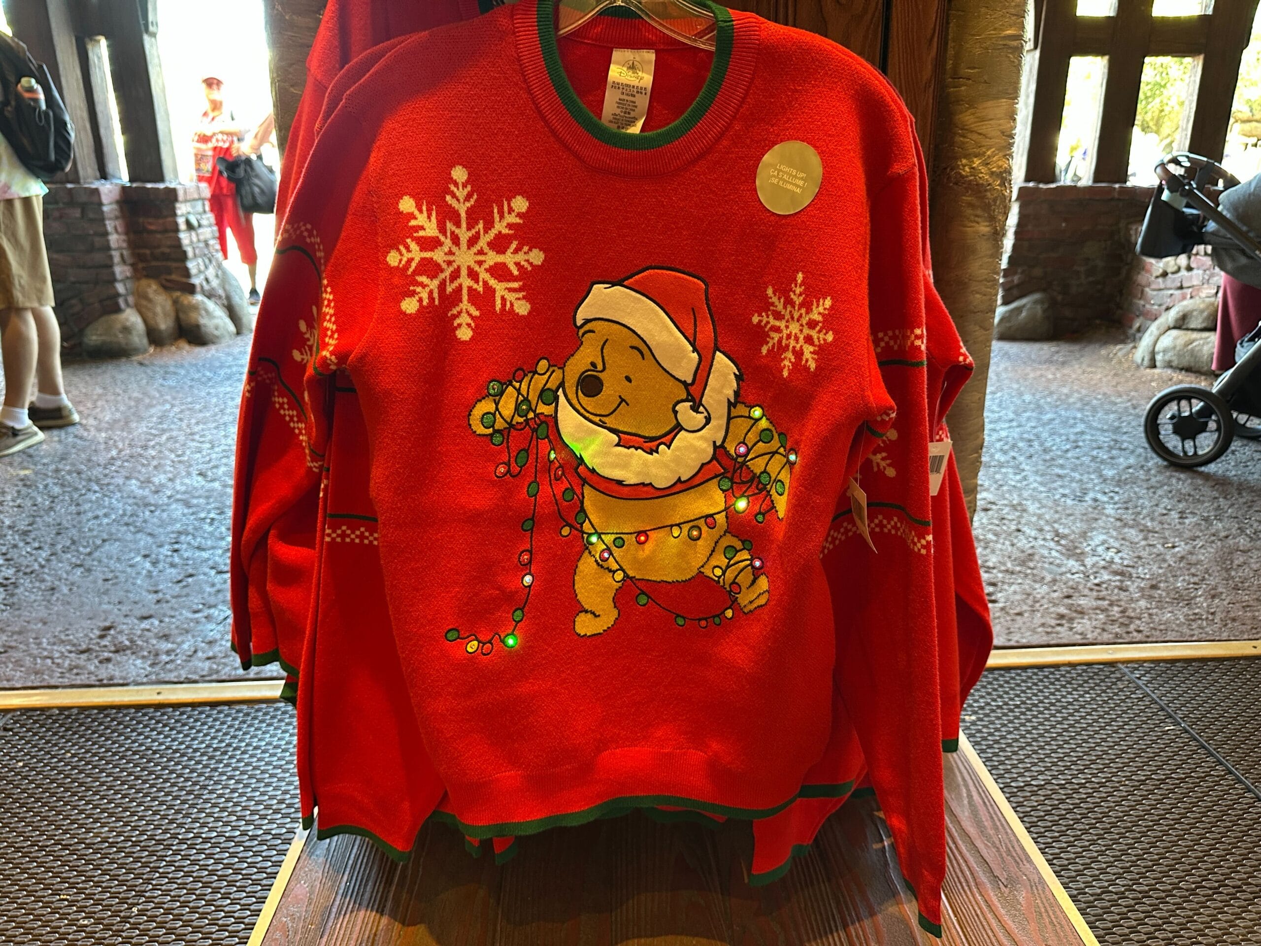 Red holiday sweater with Winnie the Pooh in a Santa hat tangled in lights, surrounded by Disney World’s iconic snowflake designs.