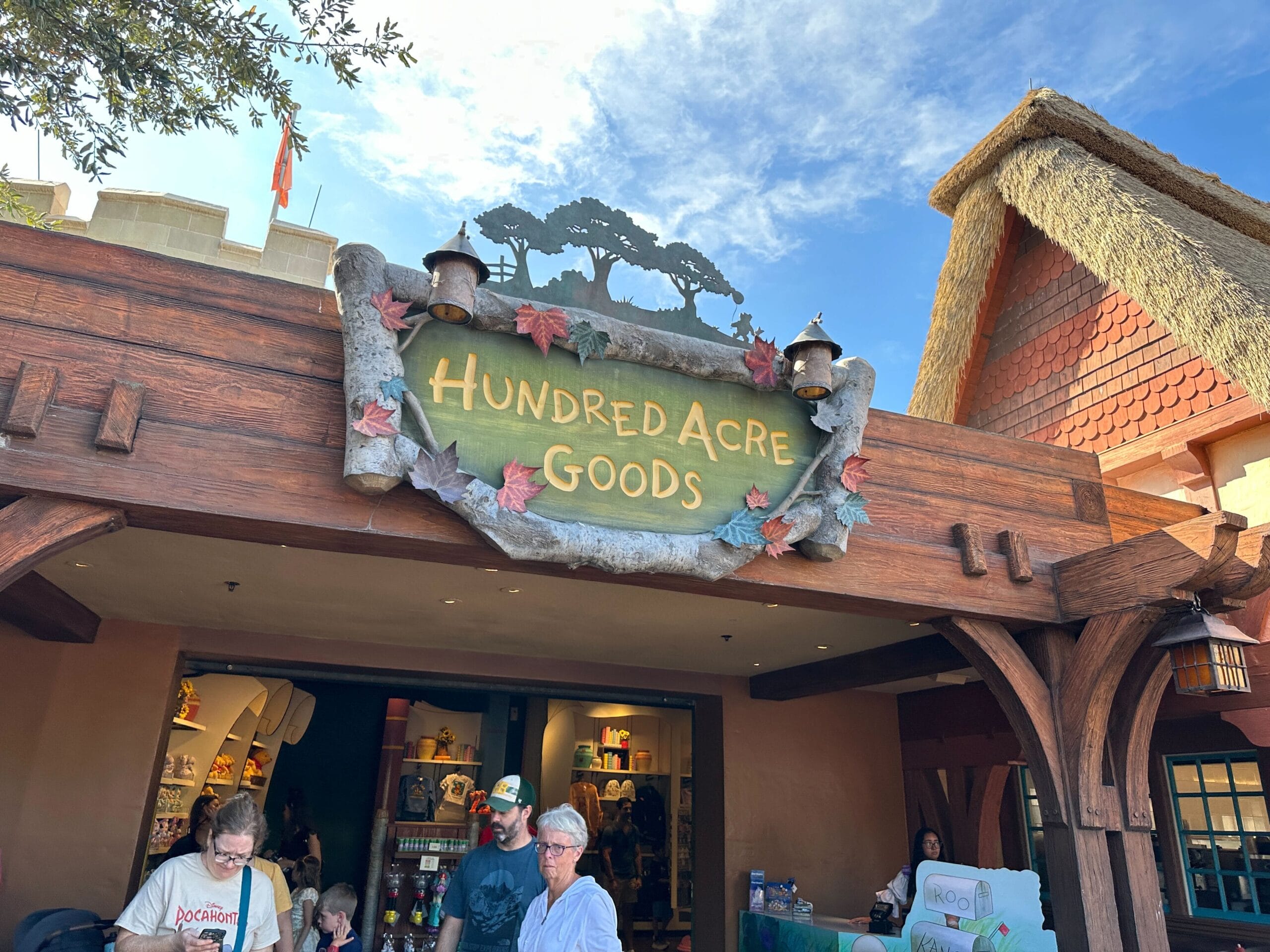 A wooden “Hundred Acre Goods” sign hangs above a Disney World shop with guests below—no castle visible to compare among the parks.