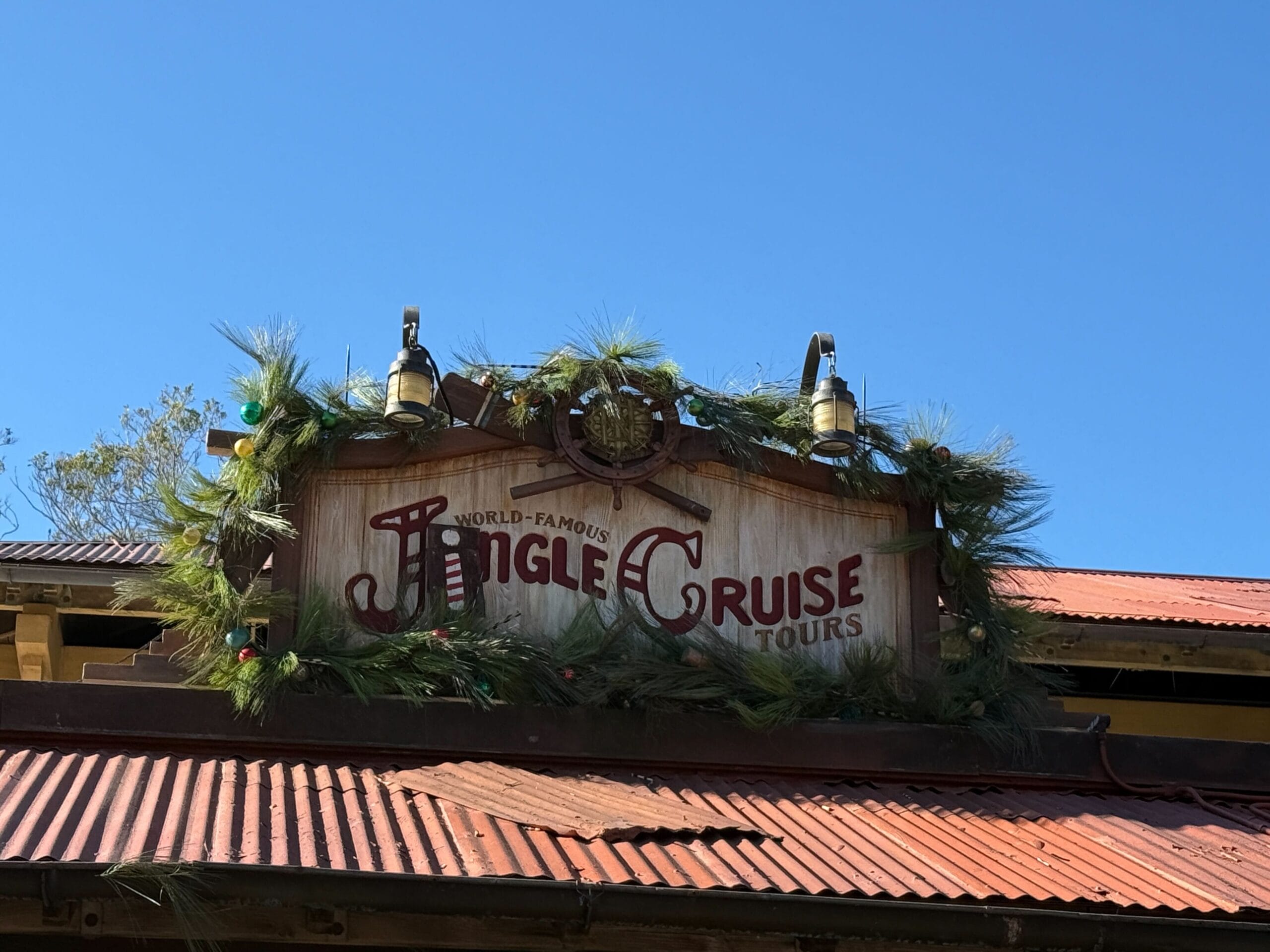 A rustic "Jingle Cruise Tours" sign with Christmas greenery glows at Magic Kingdom