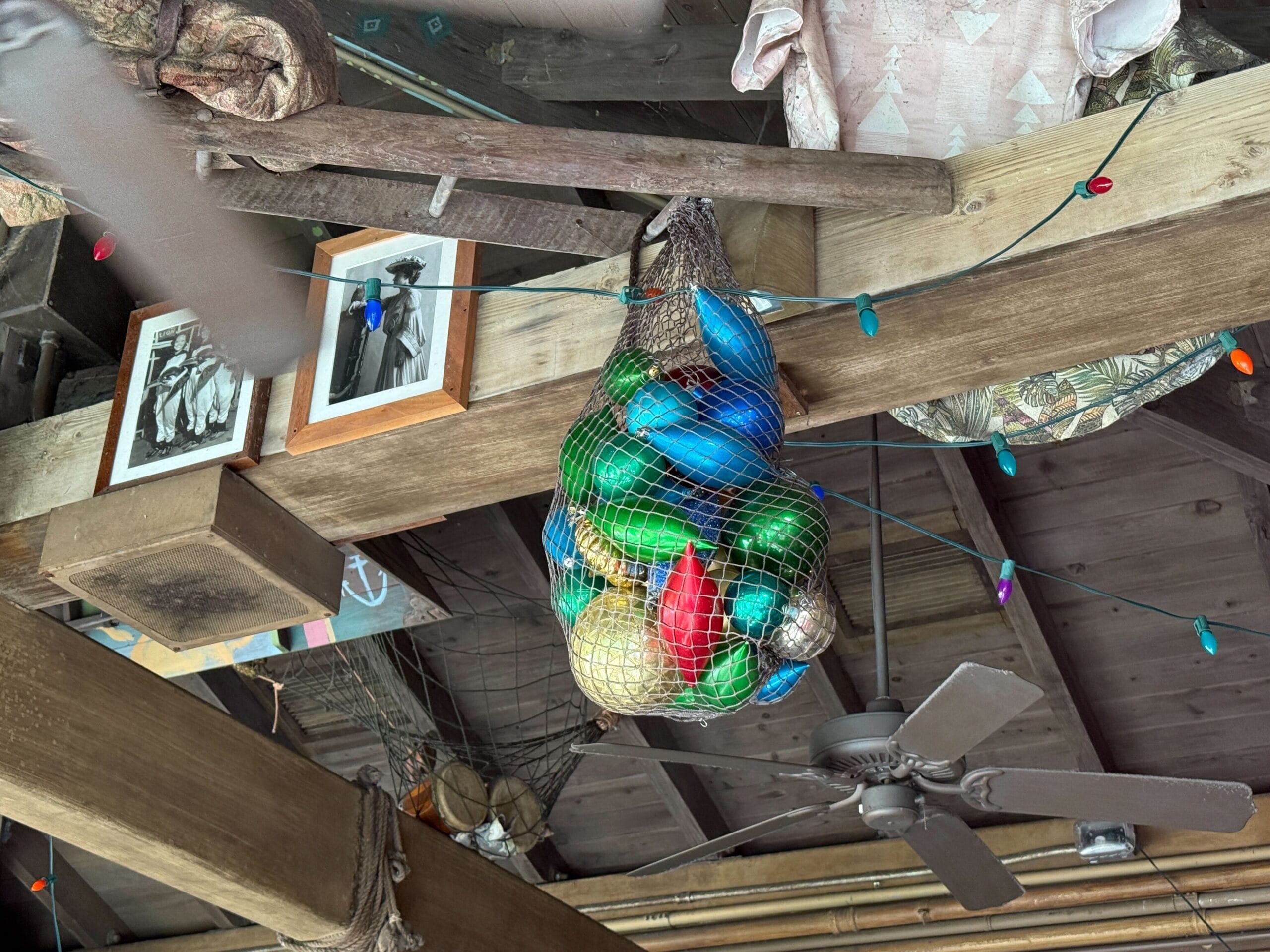A net of vibrant glass floats hangs by string lights, photos, and a fan—evoking Jingle Cruise decor at Magic Kingdom