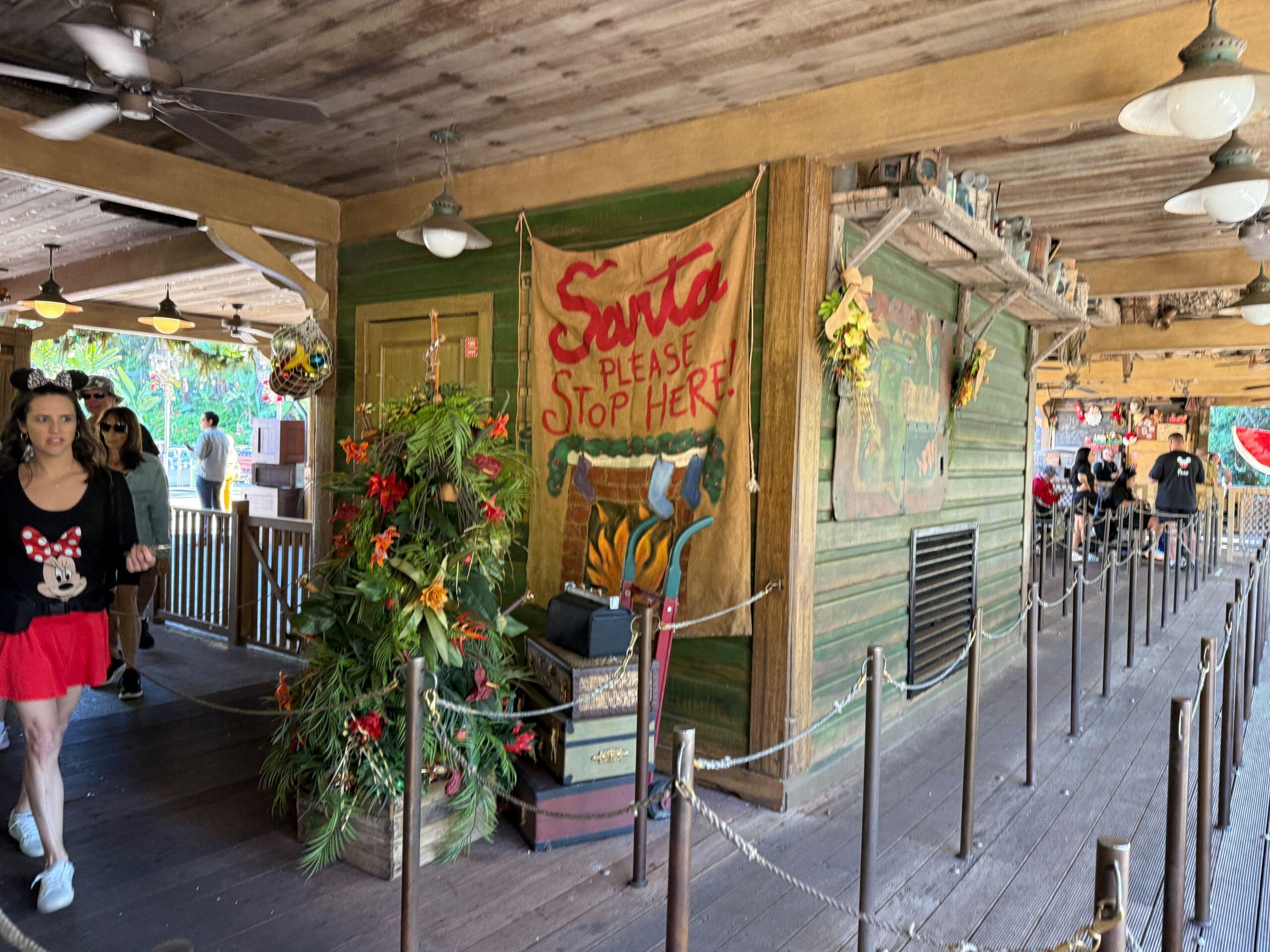 A festive "Santa Please Stop Here!" sign decorates Magic Kingdom’s Jingle Cruise queue as guests walk past