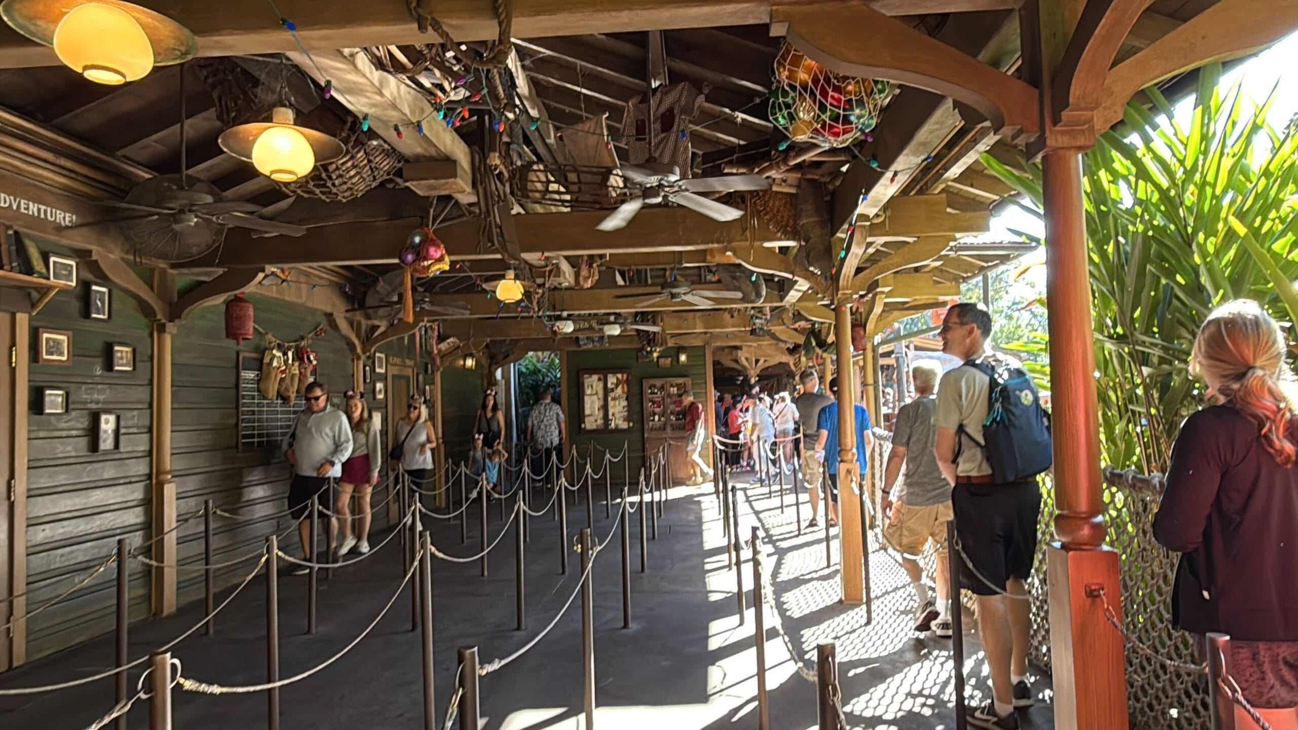 Guests line up in a festively decorated, shaded Jingle Cruise queue at Magic Kingdom, holiday details unique to Disney World.