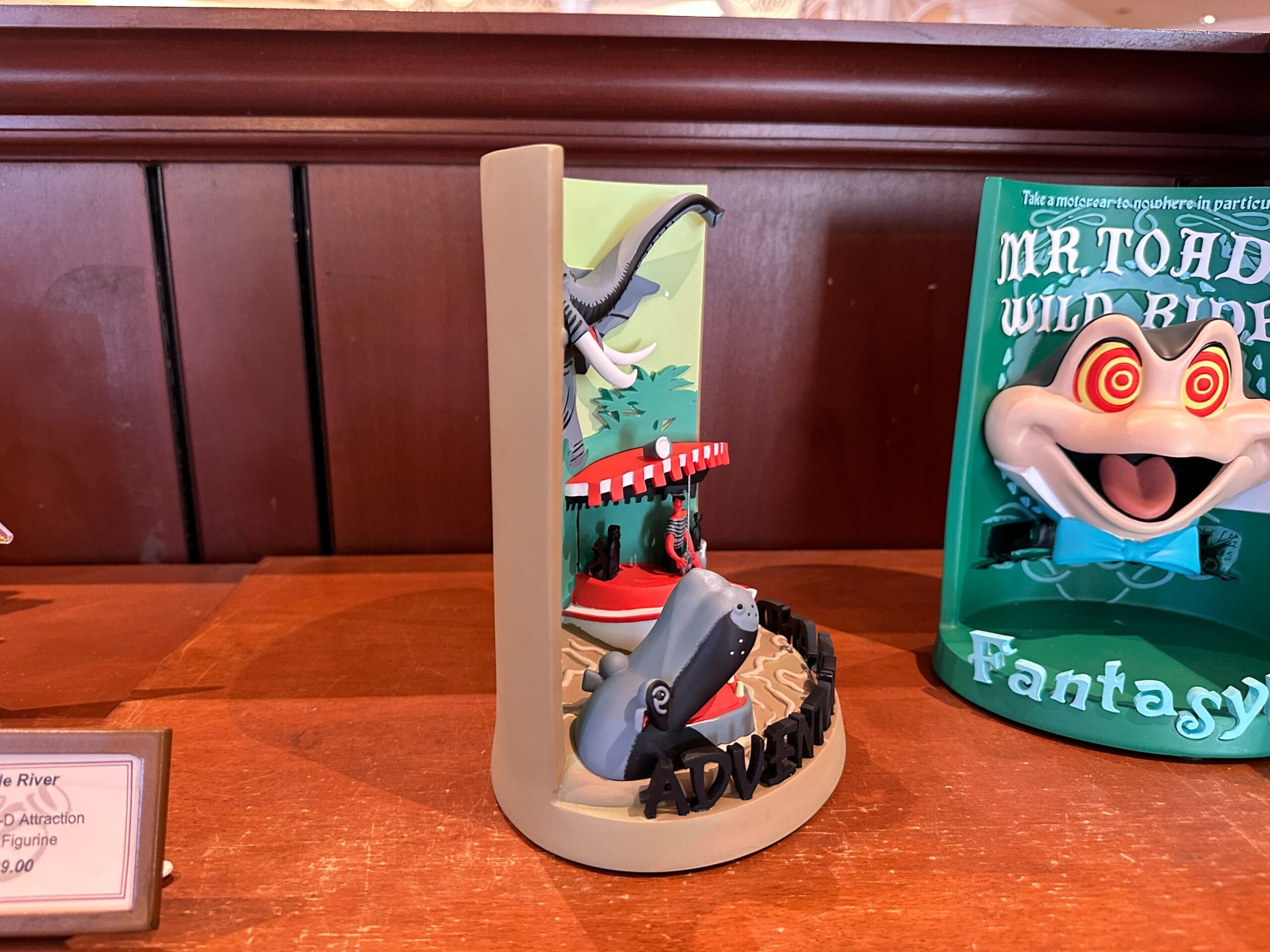 A Jungle Cruise 3-D Attraction Figurine bookend with a hippo, boat, and alligator on a wooden shelf.