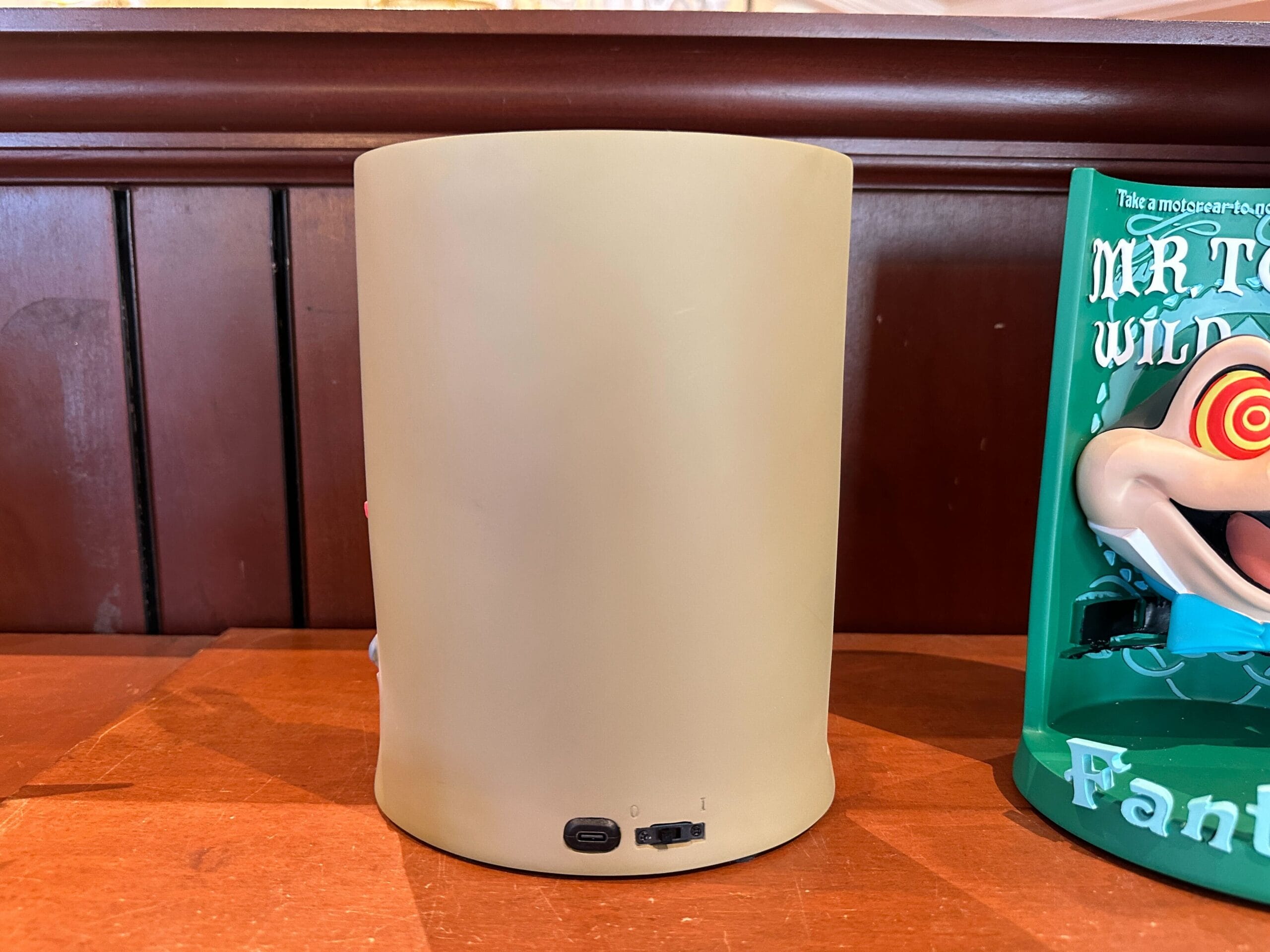 A beige cylindrical device with charging ports sits by a colorful book and a Jungle Cruise 3-D figurine.