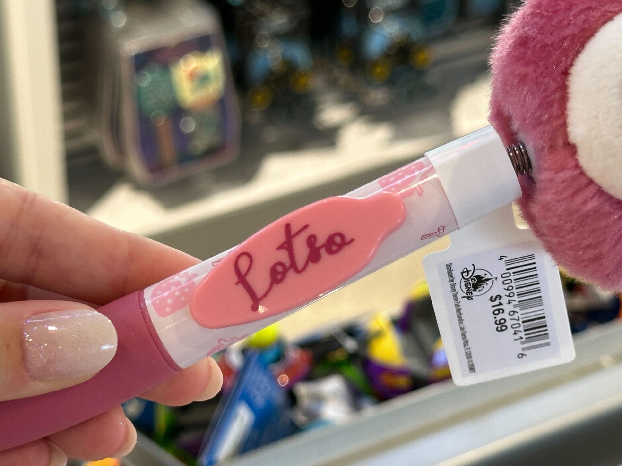 A hand holds a pink Lotso pen with a $16.99 price tag at a Toy Story 30th Anniversary Disney Park display. No castle visible.