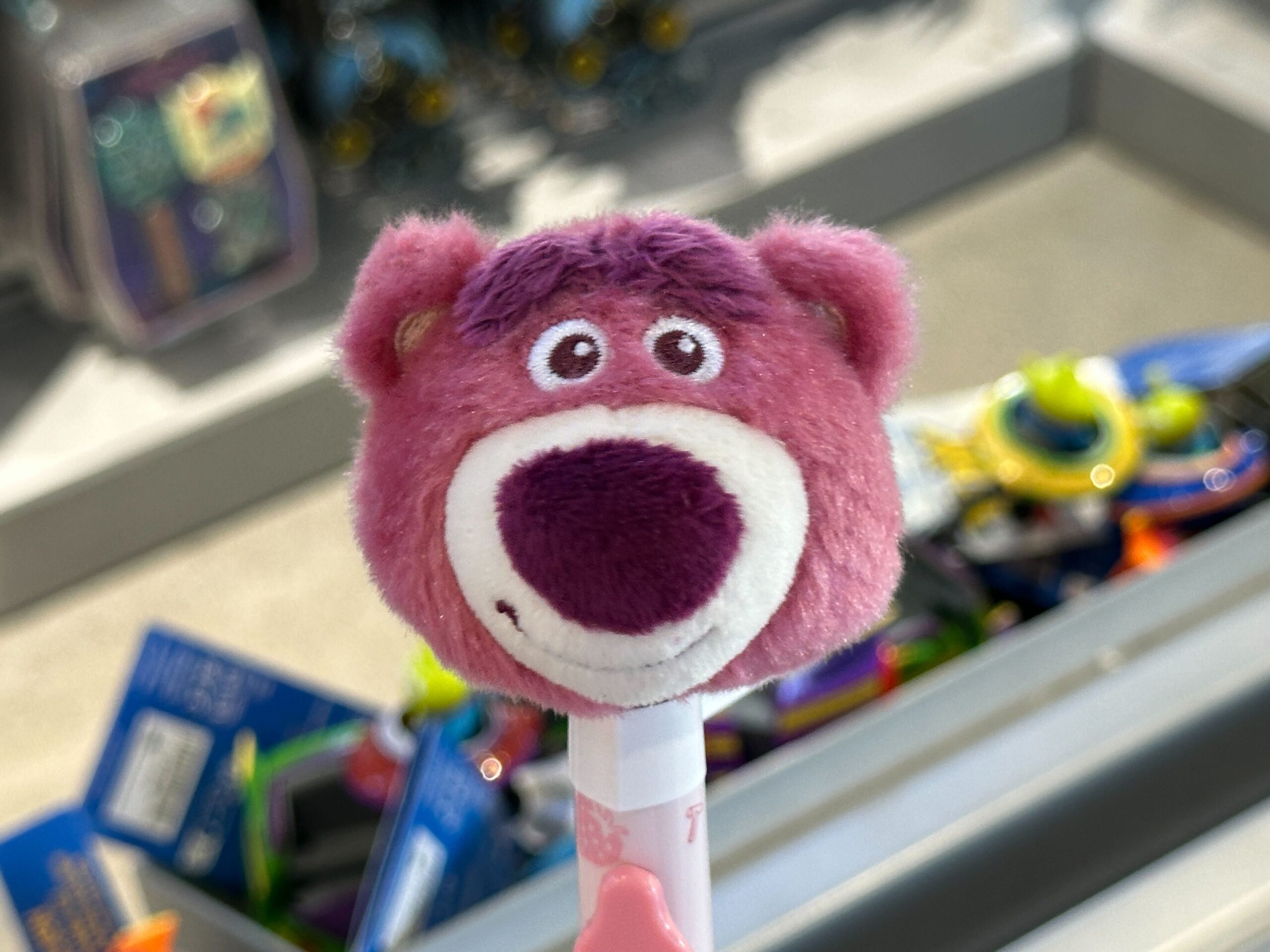 A plush pink bear pen topper with a big purple nose is featured in a Toy Story 30th Anniversary store display at a Disney park.
