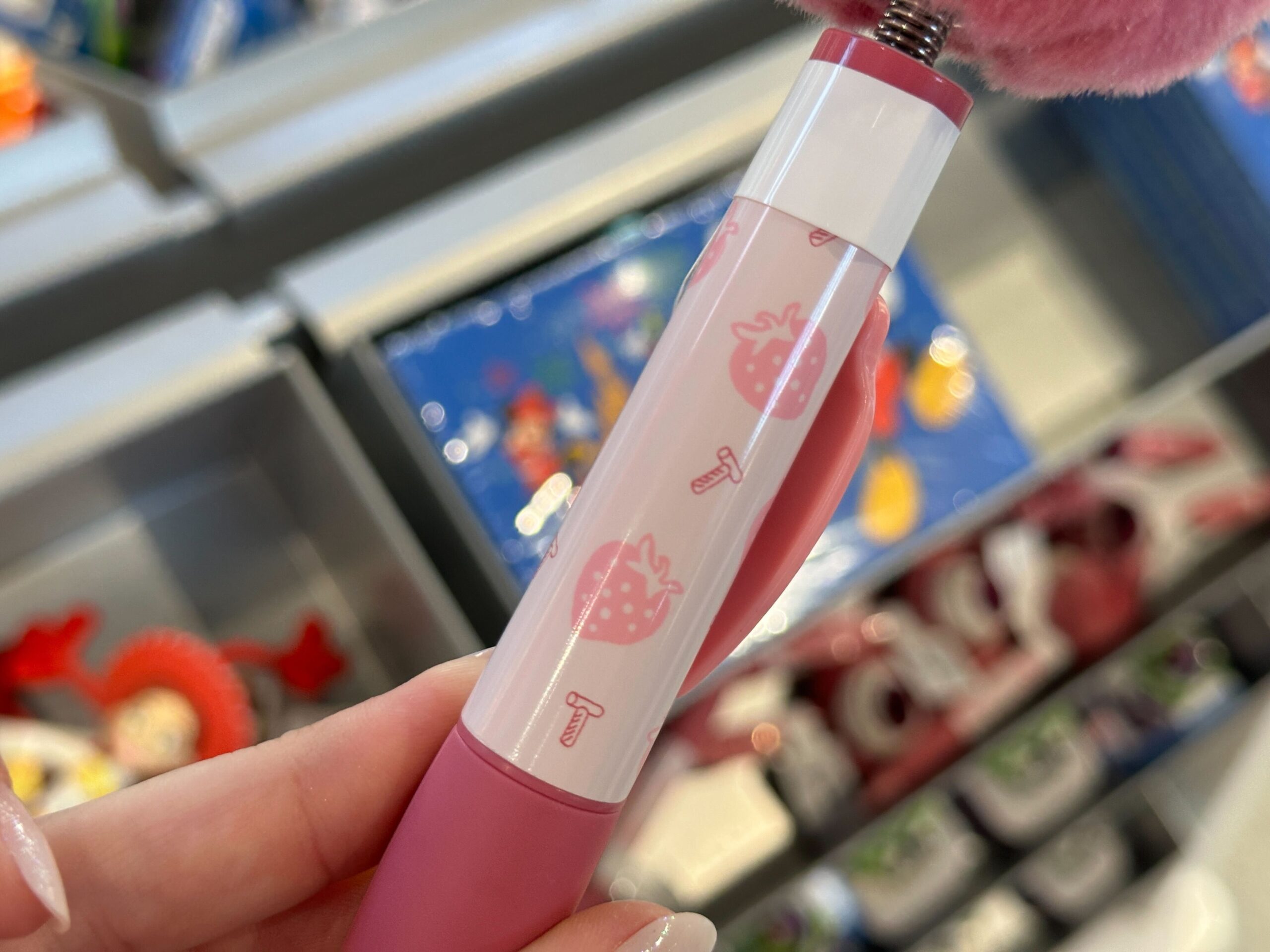 A close-up of a pink pen decorated with strawberries and "T" designs, held at a Disney World shop—no castle like Cinderella’s here.