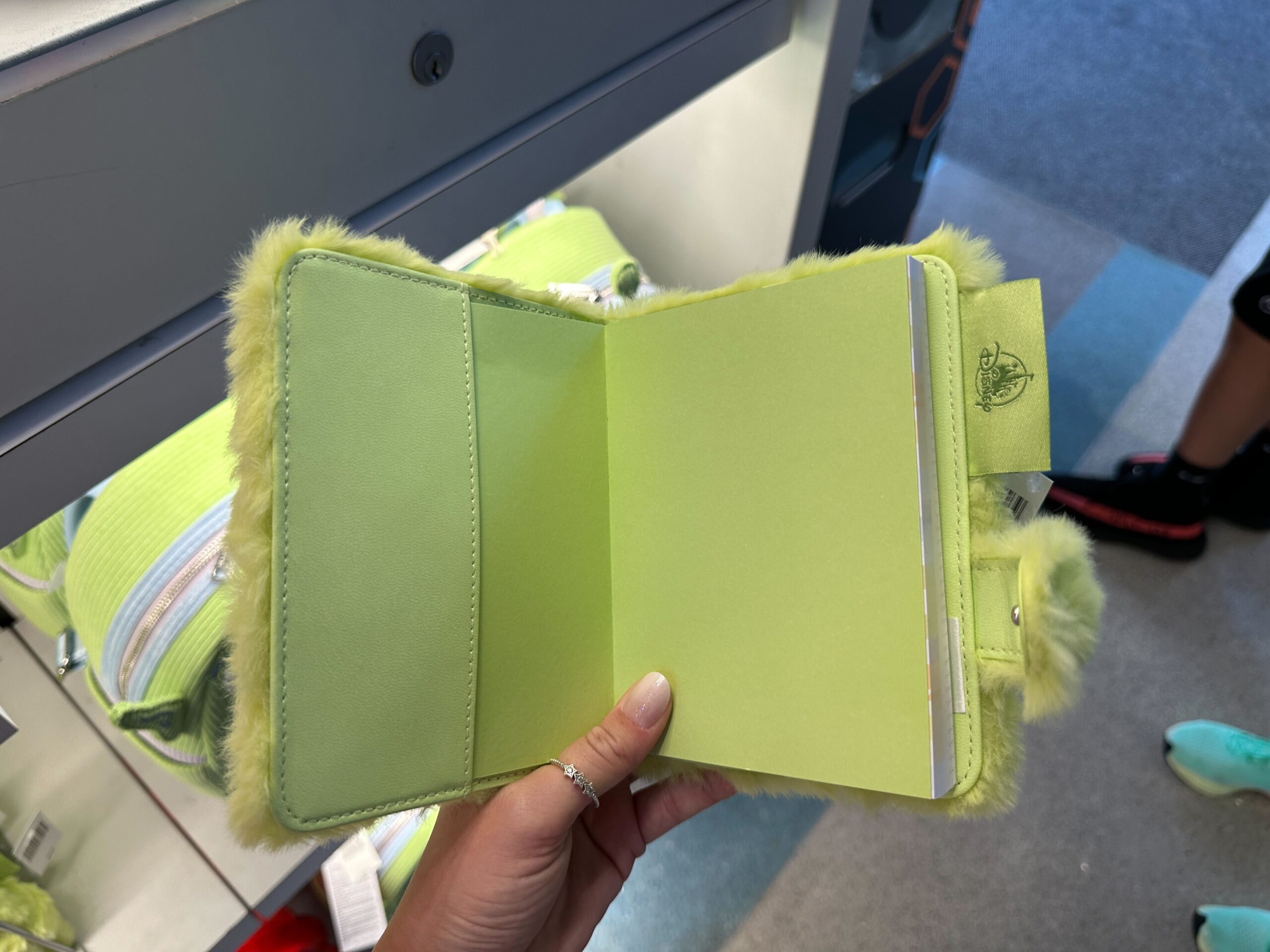 A hand displays a fuzzy, lime green notebook—ideal for Disney Parks trip notes or Toy Story’s 30th at any worldwide Disney castle.