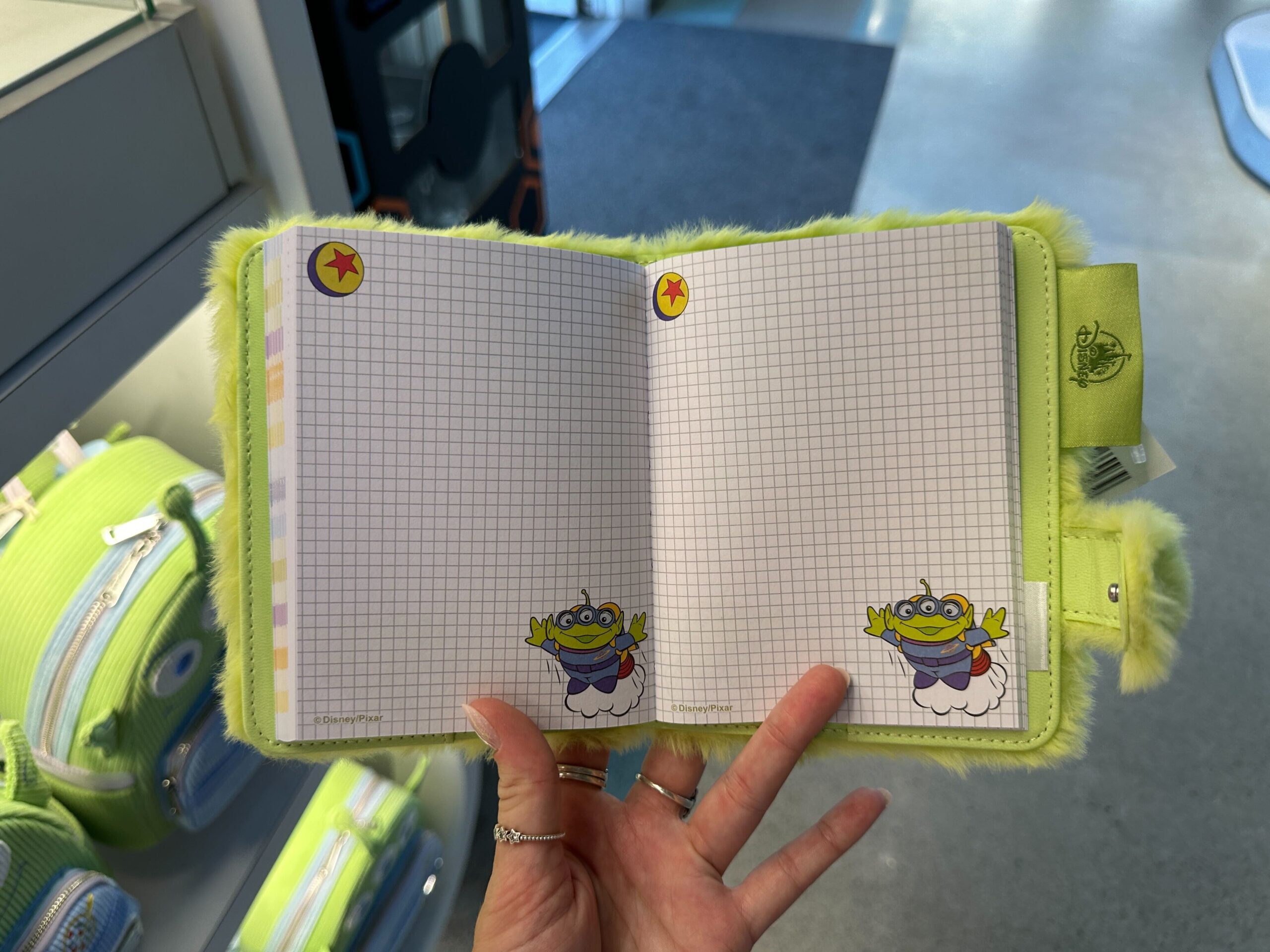 A hand displays a fuzzy Toy Story 30th Anniversary notebook with playful alien figures on graph pages, perfect for Disney Parks fans.