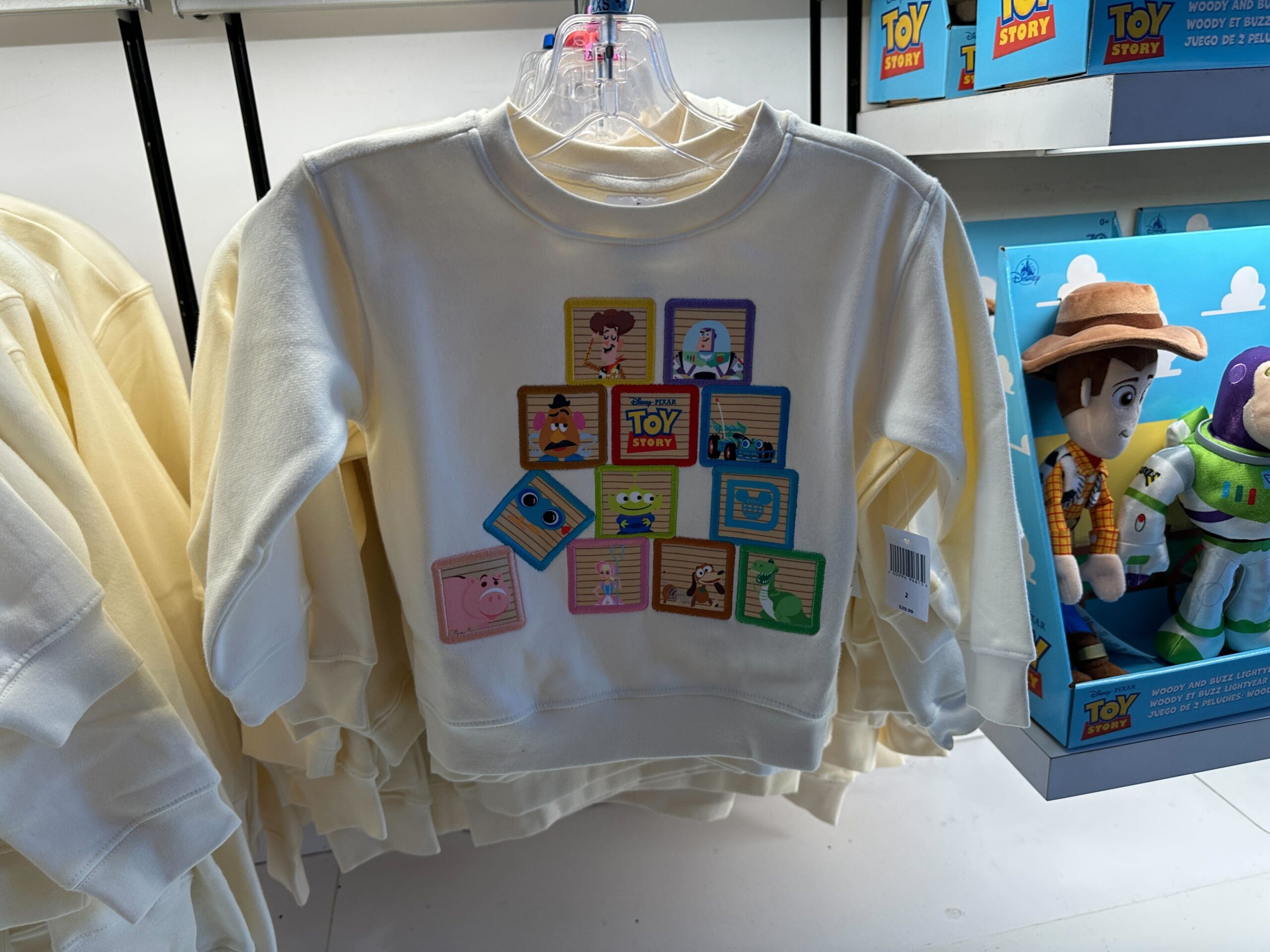 Cream Toy Story sweatshirt with vibrant character block designs, ideal for celebrating Toy Story 30th at Disney parks worldwide.